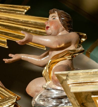 Zdjęcie nr 32: Drewniany, przyścienny ołtarz o formach architektonicznych, jednoosiowy, jednokondygnacyjny ze zwieńczeniem. Mensa murowana w kształcie prostopadłościanu zwieńczonego profilowanym gzymsem; antepedium prostokątne, w drewnianej, płaskorzeźbionej w motywy akantowe, złoconej ramie, dwustronne. Awers tłoczony, srebrzony, wykonany w technice papier mâché; rewers z malowanym na desce wyobrażeniem Veraicon na tle narzędzi męki. Tabernakulum na osi, złożone z mosiężnej, złoconej, sześciobocznej skrzynki w rozbudowanej, drewnianej obudowie o formach architektonicznych. Na nim tron wystawienia w kształcie niszy dekorowanej kratką, nakrytej kopułką z latarnią i przysłoniętej złapanymi po bokach kotarami. Na latarni rzeźbione przedstawienie pelikana karmiącego pisklęta własną krwią. Skrzynkę z tronem ulokowano na tle parawanu ustawionego na podwójnym cokole, ażurowego w górnej części, wypełnionego dekoracją roślinną, złączonego z kopułka spływami. 
Retabulum ołtarzowe drewniane wsparte na wysokim, dwudzielnym, murowanym cokole. Cokół w obudowie drewnianej, jego kondygnacje wydzielone wydatnymi, silnie występującymi przed lico gzymsami; mocno wysunięte ku przodowi części przednie. Ich lica z prostokątnymi płycinami mieszczącymi suchy akant; w części środkowej drugiej kondygnacji cokołu, dodatkowo pełnoplastyczne główki puttów. Na cokole ustawione zdwojone, złocone kolumny o skręconych trzonach i kompozytowych kapitelach. Pomiędzy nimi płyciny wypełnione dekoracją w formie podwieszonego wieńca, u jego szczytu putta pełniące rolę atlantów. Na tle płycin ustawione drewniane, złocone figury z lewej św. Zygmunta i z prawej św. Marii Magdaleny – patronów kościoła. Pole ołtarza z prostokątną niszą zamkniętą łukiem wyniesionym; ujętą płaskorzeźbioną, złoconą ramą zdobioną suchym akantem. W niszy pełnoplastyczny, polichromowany i złocony krucyfiks na aksamitnym tle, flankowany przez płaskorzeźbione wyobrażenia słońca i księżyca. Nisza zasuwana obrazem z Przemienieniem na górze Tabor, w drewnianej, złoconej sukience. Kolumny dźwigają pełne, wyłamane na osiach podpór belkowanie, z wydatnym, silnie profilowanym gzymsem; na jego osi złocony monogram „IHS” w otoku ze srebrzonych obłoków na tle promienistej glorii. Całość wieńczą fragmenty przerwanego przyczółka o formach wklęsło-wypukłych, z ażurową dekoracją z suchego akantu. Pomiędzy ramionami przyczółka złocona gloria promienista, w centrum której płaskorzeźbiona postać Boga Ojca siedzącego na srebrzonym obłoku ze srebrzoną gołębicą Ducha Świętego u stóp. Na ramionach glorii uskrzydlone główki puttów, niektóre na tle obłoków. Po bokach, na gzymsie siedzące postaci nagich, adorujących puttów. Ołtarz ujęty ażurowymi, złoconymi uszami z suchego akantu, w który wplecione są groteskowe putta trzymające pochodnie. Większość powierzchni ołtarza marmoryzowana, w kolorze jasnej, oliwkowej zieleni, z ciemniejszymi brązowymi elementami wypełniającymi płyciny. Złocenia w partiach ornamentów, kolumn oraz załamaniach profili elementów architektonicznych; srebrzone obłoki, części szat postaci i pelikan. 