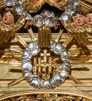 Zdjęcie nr 31: Drewniany, przyścienny ołtarz o formach architektonicznych, jednoosiowy, jednokondygnacyjny ze zwieńczeniem. Mensa murowana w kształcie prostopadłościanu zwieńczonego profilowanym gzymsem; antepedium prostokątne, w drewnianej, płaskorzeźbionej w motywy akantowe, złoconej ramie, dwustronne. Awers tłoczony, srebrzony, wykonany w technice papier mâché; rewers z malowanym na desce wyobrażeniem Veraicon na tle narzędzi męki. Tabernakulum na osi, złożone z mosiężnej, złoconej, sześciobocznej skrzynki w rozbudowanej, drewnianej obudowie o formach architektonicznych. Na nim tron wystawienia w kształcie niszy dekorowanej kratką, nakrytej kopułką z latarnią i przysłoniętej złapanymi po bokach kotarami. Na latarni rzeźbione przedstawienie pelikana karmiącego pisklęta własną krwią. Skrzynkę z tronem ulokowano na tle parawanu ustawionego na podwójnym cokole, ażurowego w górnej części, wypełnionego dekoracją roślinną, złączonego z kopułka spływami. 
Retabulum ołtarzowe drewniane wsparte na wysokim, dwudzielnym, murowanym cokole. Cokół w obudowie drewnianej, jego kondygnacje wydzielone wydatnymi, silnie występującymi przed lico gzymsami; mocno wysunięte ku przodowi części przednie. Ich lica z prostokątnymi płycinami mieszczącymi suchy akant; w części środkowej drugiej kondygnacji cokołu, dodatkowo pełnoplastyczne główki puttów. Na cokole ustawione zdwojone, złocone kolumny o skręconych trzonach i kompozytowych kapitelach. Pomiędzy nimi płyciny wypełnione dekoracją w formie podwieszonego wieńca, u jego szczytu putta pełniące rolę atlantów. Na tle płycin ustawione drewniane, złocone figury z lewej św. Zygmunta i z prawej św. Marii Magdaleny – patronów kościoła. Pole ołtarza z prostokątną niszą zamkniętą łukiem wyniesionym; ujętą płaskorzeźbioną, złoconą ramą zdobioną suchym akantem. W niszy pełnoplastyczny, polichromowany i złocony krucyfiks na aksamitnym tle, flankowany przez płaskorzeźbione wyobrażenia słońca i księżyca. Nisza zasuwana obrazem z Przemienieniem na górze Tabor, w drewnianej, złoconej sukience. Kolumny dźwigają pełne, wyłamane na osiach podpór belkowanie, z wydatnym, silnie profilowanym gzymsem; na jego osi złocony monogram „IHS” w otoku ze srebrzonych obłoków na tle promienistej glorii. Całość wieńczą fragmenty przerwanego przyczółka o formach wklęsło-wypukłych, z ażurową dekoracją z suchego akantu. Pomiędzy ramionami przyczółka złocona gloria promienista, w centrum której płaskorzeźbiona postać Boga Ojca siedzącego na srebrzonym obłoku ze srebrzoną gołębicą Ducha Świętego u stóp. Na ramionach glorii uskrzydlone główki puttów, niektóre na tle obłoków. Po bokach, na gzymsie siedzące postaci nagich, adorujących puttów. Ołtarz ujęty ażurowymi, złoconymi uszami z suchego akantu, w który wplecione są groteskowe putta trzymające pochodnie. Większość powierzchni ołtarza marmoryzowana, w kolorze jasnej, oliwkowej zieleni, z ciemniejszymi brązowymi elementami wypełniającymi płyciny. Złocenia w partiach ornamentów, kolumn oraz załamaniach profili elementów architektonicznych; srebrzone obłoki, części szat postaci i pelikan. 