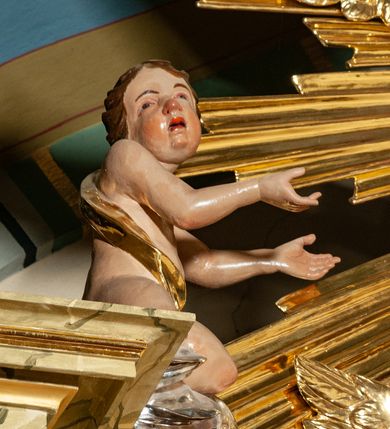 Zdjęcie nr 33: Drewniany, przyścienny ołtarz o formach architektonicznych, jednoosiowy, jednokondygnacyjny ze zwieńczeniem. Mensa murowana w kształcie prostopadłościanu zwieńczonego profilowanym gzymsem; antepedium prostokątne, w drewnianej, płaskorzeźbionej w motywy akantowe, złoconej ramie, dwustronne. Awers tłoczony, srebrzony, wykonany w technice papier mâché; rewers z malowanym na desce wyobrażeniem Veraicon na tle narzędzi męki. Tabernakulum na osi, złożone z mosiężnej, złoconej, sześciobocznej skrzynki w rozbudowanej, drewnianej obudowie o formach architektonicznych. Na nim tron wystawienia w kształcie niszy dekorowanej kratką, nakrytej kopułką z latarnią i przysłoniętej złapanymi po bokach kotarami. Na latarni rzeźbione przedstawienie pelikana karmiącego pisklęta własną krwią. Skrzynkę z tronem ulokowano na tle parawanu ustawionego na podwójnym cokole, ażurowego w górnej części, wypełnionego dekoracją roślinną, złączonego z kopułka spływami. 
Retabulum ołtarzowe drewniane wsparte na wysokim, dwudzielnym, murowanym cokole. Cokół w obudowie drewnianej, jego kondygnacje wydzielone wydatnymi, silnie występującymi przed lico gzymsami; mocno wysunięte ku przodowi części przednie. Ich lica z prostokątnymi płycinami mieszczącymi suchy akant; w części środkowej drugiej kondygnacji cokołu, dodatkowo pełnoplastyczne główki puttów. Na cokole ustawione zdwojone, złocone kolumny o skręconych trzonach i kompozytowych kapitelach. Pomiędzy nimi płyciny wypełnione dekoracją w formie podwieszonego wieńca, u jego szczytu putta pełniące rolę atlantów. Na tle płycin ustawione drewniane, złocone figury z lewej św. Zygmunta i z prawej św. Marii Magdaleny – patronów kościoła. Pole ołtarza z prostokątną niszą zamkniętą łukiem wyniesionym; ujętą płaskorzeźbioną, złoconą ramą zdobioną suchym akantem. W niszy pełnoplastyczny, polichromowany i złocony krucyfiks na aksamitnym tle, flankowany przez płaskorzeźbione wyobrażenia słońca i księżyca. Nisza zasuwana obrazem z Przemienieniem na górze Tabor, w drewnianej, złoconej sukience. Kolumny dźwigają pełne, wyłamane na osiach podpór belkowanie, z wydatnym, silnie profilowanym gzymsem; na jego osi złocony monogram „IHS” w otoku ze srebrzonych obłoków na tle promienistej glorii. Całość wieńczą fragmenty przerwanego przyczółka o formach wklęsło-wypukłych, z ażurową dekoracją z suchego akantu. Pomiędzy ramionami przyczółka złocona gloria promienista, w centrum której płaskorzeźbiona postać Boga Ojca siedzącego na srebrzonym obłoku ze srebrzoną gołębicą Ducha Świętego u stóp. Na ramionach glorii uskrzydlone główki puttów, niektóre na tle obłoków. Po bokach, na gzymsie siedzące postaci nagich, adorujących puttów. Ołtarz ujęty ażurowymi, złoconymi uszami z suchego akantu, w który wplecione są groteskowe putta trzymające pochodnie. Większość powierzchni ołtarza marmoryzowana, w kolorze jasnej, oliwkowej zieleni, z ciemniejszymi brązowymi elementami wypełniającymi płyciny. Złocenia w partiach ornamentów, kolumn oraz załamaniach profili elementów architektonicznych; srebrzone obłoki, części szat postaci i pelikan. 