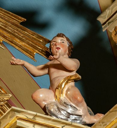 Zdjęcie nr 35: Drewniany, przyścienny ołtarz o formach architektonicznych, jednoosiowy, jednokondygnacyjny ze zwieńczeniem. Mensa murowana w kształcie prostopadłościanu zwieńczonego profilowanym gzymsem; antepedium prostokątne, w drewnianej, płaskorzeźbionej w motywy akantowe, złoconej ramie, dwustronne. Awers tłoczony, srebrzony, wykonany w technice papier mâché; rewers z malowanym na desce wyobrażeniem Veraicon na tle narzędzi męki. Tabernakulum na osi, złożone z mosiężnej, złoconej, sześciobocznej skrzynki w rozbudowanej, drewnianej obudowie o formach architektonicznych. Na nim tron wystawienia w kształcie niszy dekorowanej kratką, nakrytej kopułką z latarnią i przysłoniętej złapanymi po bokach kotarami. Na latarni rzeźbione przedstawienie pelikana karmiącego pisklęta własną krwią. Skrzynkę z tronem ulokowano na tle parawanu ustawionego na podwójnym cokole, ażurowego w górnej części, wypełnionego dekoracją roślinną, złączonego z kopułka spływami. 
Retabulum ołtarzowe drewniane wsparte na wysokim, dwudzielnym, murowanym cokole. Cokół w obudowie drewnianej, jego kondygnacje wydzielone wydatnymi, silnie występującymi przed lico gzymsami; mocno wysunięte ku przodowi części przednie. Ich lica z prostokątnymi płycinami mieszczącymi suchy akant; w części środkowej drugiej kondygnacji cokołu, dodatkowo pełnoplastyczne główki puttów. Na cokole ustawione zdwojone, złocone kolumny o skręconych trzonach i kompozytowych kapitelach. Pomiędzy nimi płyciny wypełnione dekoracją w formie podwieszonego wieńca, u jego szczytu putta pełniące rolę atlantów. Na tle płycin ustawione drewniane, złocone figury z lewej św. Zygmunta i z prawej św. Marii Magdaleny – patronów kościoła. Pole ołtarza z prostokątną niszą zamkniętą łukiem wyniesionym; ujętą płaskorzeźbioną, złoconą ramą zdobioną suchym akantem. W niszy pełnoplastyczny, polichromowany i złocony krucyfiks na aksamitnym tle, flankowany przez płaskorzeźbione wyobrażenia słońca i księżyca. Nisza zasuwana obrazem z Przemienieniem na górze Tabor, w drewnianej, złoconej sukience. Kolumny dźwigają pełne, wyłamane na osiach podpór belkowanie, z wydatnym, silnie profilowanym gzymsem; na jego osi złocony monogram „IHS” w otoku ze srebrzonych obłoków na tle promienistej glorii. Całość wieńczą fragmenty przerwanego przyczółka o formach wklęsło-wypukłych, z ażurową dekoracją z suchego akantu. Pomiędzy ramionami przyczółka złocona gloria promienista, w centrum której płaskorzeźbiona postać Boga Ojca siedzącego na srebrzonym obłoku ze srebrzoną gołębicą Ducha Świętego u stóp. Na ramionach glorii uskrzydlone główki puttów, niektóre na tle obłoków. Po bokach, na gzymsie siedzące postaci nagich, adorujących puttów. Ołtarz ujęty ażurowymi, złoconymi uszami z suchego akantu, w który wplecione są groteskowe putta trzymające pochodnie. Większość powierzchni ołtarza marmoryzowana, w kolorze jasnej, oliwkowej zieleni, z ciemniejszymi brązowymi elementami wypełniającymi płyciny. Złocenia w partiach ornamentów, kolumn oraz załamaniach profili elementów architektonicznych; srebrzone obłoki, części szat postaci i pelikan. 