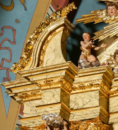 Zdjęcie nr 36: Drewniany, przyścienny ołtarz o formach architektonicznych, jednoosiowy, jednokondygnacyjny ze zwieńczeniem. Mensa murowana w kształcie prostopadłościanu zwieńczonego profilowanym gzymsem; antepedium prostokątne, w drewnianej, płaskorzeźbionej w motywy akantowe, złoconej ramie, dwustronne. Awers tłoczony, srebrzony, wykonany w technice papier mâché; rewers z malowanym na desce wyobrażeniem Veraicon na tle narzędzi męki. Tabernakulum na osi, złożone z mosiężnej, złoconej, sześciobocznej skrzynki w rozbudowanej, drewnianej obudowie o formach architektonicznych. Na nim tron wystawienia w kształcie niszy dekorowanej kratką, nakrytej kopułką z latarnią i przysłoniętej złapanymi po bokach kotarami. Na latarni rzeźbione przedstawienie pelikana karmiącego pisklęta własną krwią. Skrzynkę z tronem ulokowano na tle parawanu ustawionego na podwójnym cokole, ażurowego w górnej części, wypełnionego dekoracją roślinną, złączonego z kopułka spływami. 
Retabulum ołtarzowe drewniane wsparte na wysokim, dwudzielnym, murowanym cokole. Cokół w obudowie drewnianej, jego kondygnacje wydzielone wydatnymi, silnie występującymi przed lico gzymsami; mocno wysunięte ku przodowi części przednie. Ich lica z prostokątnymi płycinami mieszczącymi suchy akant; w części środkowej drugiej kondygnacji cokołu, dodatkowo pełnoplastyczne główki puttów. Na cokole ustawione zdwojone, złocone kolumny o skręconych trzonach i kompozytowych kapitelach. Pomiędzy nimi płyciny wypełnione dekoracją w formie podwieszonego wieńca, u jego szczytu putta pełniące rolę atlantów. Na tle płycin ustawione drewniane, złocone figury z lewej św. Zygmunta i z prawej św. Marii Magdaleny – patronów kościoła. Pole ołtarza z prostokątną niszą zamkniętą łukiem wyniesionym; ujętą płaskorzeźbioną, złoconą ramą zdobioną suchym akantem. W niszy pełnoplastyczny, polichromowany i złocony krucyfiks na aksamitnym tle, flankowany przez płaskorzeźbione wyobrażenia słońca i księżyca. Nisza zasuwana obrazem z Przemienieniem na górze Tabor, w drewnianej, złoconej sukience. Kolumny dźwigają pełne, wyłamane na osiach podpór belkowanie, z wydatnym, silnie profilowanym gzymsem; na jego osi złocony monogram „IHS” w otoku ze srebrzonych obłoków na tle promienistej glorii. Całość wieńczą fragmenty przerwanego przyczółka o formach wklęsło-wypukłych, z ażurową dekoracją z suchego akantu. Pomiędzy ramionami przyczółka złocona gloria promienista, w centrum której płaskorzeźbiona postać Boga Ojca siedzącego na srebrzonym obłoku ze srebrzoną gołębicą Ducha Świętego u stóp. Na ramionach glorii uskrzydlone główki puttów, niektóre na tle obłoków. Po bokach, na gzymsie siedzące postaci nagich, adorujących puttów. Ołtarz ujęty ażurowymi, złoconymi uszami z suchego akantu, w który wplecione są groteskowe putta trzymające pochodnie. Większość powierzchni ołtarza marmoryzowana, w kolorze jasnej, oliwkowej zieleni, z ciemniejszymi brązowymi elementami wypełniającymi płyciny. Złocenia w partiach ornamentów, kolumn oraz załamaniach profili elementów architektonicznych; srebrzone obłoki, części szat postaci i pelikan. 