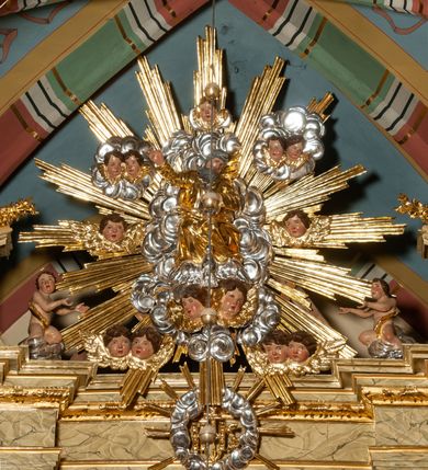 Zdjęcie nr 49: Drewniany, przyścienny ołtarz o formach architektonicznych, jednoosiowy, jednokondygnacyjny ze zwieńczeniem. Mensa murowana w kształcie prostopadłościanu zwieńczonego profilowanym gzymsem; antepedium prostokątne, w drewnianej, płaskorzeźbionej w motywy akantowe, złoconej ramie, dwustronne. Awers tłoczony, srebrzony, wykonany w technice papier mâché; rewers z malowanym na desce wyobrażeniem Veraicon na tle narzędzi męki. Tabernakulum na osi, złożone z mosiężnej, złoconej, sześciobocznej skrzynki w rozbudowanej, drewnianej obudowie o formach architektonicznych. Na nim tron wystawienia w kształcie niszy dekorowanej kratką, nakrytej kopułką z latarnią i przysłoniętej złapanymi po bokach kotarami. Na latarni rzeźbione przedstawienie pelikana karmiącego pisklęta własną krwią. Skrzynkę z tronem ulokowano na tle parawanu ustawionego na podwójnym cokole, ażurowego w górnej części, wypełnionego dekoracją roślinną, złączonego z kopułka spływami. 
Retabulum ołtarzowe drewniane wsparte na wysokim, dwudzielnym, murowanym cokole. Cokół w obudowie drewnianej, jego kondygnacje wydzielone wydatnymi, silnie występującymi przed lico gzymsami; mocno wysunięte ku przodowi części przednie. Ich lica z prostokątnymi płycinami mieszczącymi suchy akant; w części środkowej drugiej kondygnacji cokołu, dodatkowo pełnoplastyczne główki puttów. Na cokole ustawione zdwojone, złocone kolumny o skręconych trzonach i kompozytowych kapitelach. Pomiędzy nimi płyciny wypełnione dekoracją w formie podwieszonego wieńca, u jego szczytu putta pełniące rolę atlantów. Na tle płycin ustawione drewniane, złocone figury z lewej św. Zygmunta i z prawej św. Marii Magdaleny – patronów kościoła. Pole ołtarza z prostokątną niszą zamkniętą łukiem wyniesionym; ujętą płaskorzeźbioną, złoconą ramą zdobioną suchym akantem. W niszy pełnoplastyczny, polichromowany i złocony krucyfiks na aksamitnym tle, flankowany przez płaskorzeźbione wyobrażenia słońca i księżyca. Nisza zasuwana obrazem z Przemienieniem na górze Tabor, w drewnianej, złoconej sukience. Kolumny dźwigają pełne, wyłamane na osiach podpór belkowanie, z wydatnym, silnie profilowanym gzymsem; na jego osi złocony monogram „IHS” w otoku ze srebrzonych obłoków na tle promienistej glorii. Całość wieńczą fragmenty przerwanego przyczółka o formach wklęsło-wypukłych, z ażurową dekoracją z suchego akantu. Pomiędzy ramionami przyczółka złocona gloria promienista, w centrum której płaskorzeźbiona postać Boga Ojca siedzącego na srebrzonym obłoku ze srebrzoną gołębicą Ducha Świętego u stóp. Na ramionach glorii uskrzydlone główki puttów, niektóre na tle obłoków. Po bokach, na gzymsie siedzące postaci nagich, adorujących puttów. Ołtarz ujęty ażurowymi, złoconymi uszami z suchego akantu, w który wplecione są groteskowe putta trzymające pochodnie. Większość powierzchni ołtarza marmoryzowana, w kolorze jasnej, oliwkowej zieleni, z ciemniejszymi brązowymi elementami wypełniającymi płyciny. Złocenia w partiach ornamentów, kolumn oraz załamaniach profili elementów architektonicznych; srebrzone obłoki, części szat postaci i pelikan. 