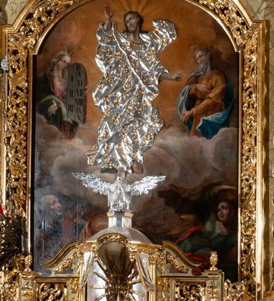 Zdjęcie nr 76: Drewniany, przyścienny ołtarz o formach architektonicznych, jednoosiowy, jednokondygnacyjny ze zwieńczeniem. Mensa murowana w kształcie prostopadłościanu zwieńczonego profilowanym gzymsem; antepedium prostokątne, w drewnianej, płaskorzeźbionej w motywy akantowe, złoconej ramie, dwustronne. Awers tłoczony, srebrzony, wykonany w technice papier mâché; rewers z malowanym na desce wyobrażeniem Veraicon na tle narzędzi męki. Tabernakulum na osi, złożone z mosiężnej, złoconej, sześciobocznej skrzynki w rozbudowanej, drewnianej obudowie o formach architektonicznych. Na nim tron wystawienia w kształcie niszy dekorowanej kratką, nakrytej kopułką z latarnią i przysłoniętej złapanymi po bokach kotarami. Na latarni rzeźbione przedstawienie pelikana karmiącego pisklęta własną krwią. Skrzynkę z tronem ulokowano na tle parawanu ustawionego na podwójnym cokole, ażurowego w górnej części, wypełnionego dekoracją roślinną, złączonego z kopułka spływami. 
Retabulum ołtarzowe drewniane wsparte na wysokim, dwudzielnym, murowanym cokole. Cokół w obudowie drewnianej, jego kondygnacje wydzielone wydatnymi, silnie występującymi przed lico gzymsami; mocno wysunięte ku przodowi części przednie. Ich lica z prostokątnymi płycinami mieszczącymi suchy akant; w części środkowej drugiej kondygnacji cokołu, dodatkowo pełnoplastyczne główki puttów. Na cokole ustawione zdwojone, złocone kolumny o skręconych trzonach i kompozytowych kapitelach. Pomiędzy nimi płyciny wypełnione dekoracją w formie podwieszonego wieńca, u jego szczytu putta pełniące rolę atlantów. Na tle płycin ustawione drewniane, złocone figury z lewej św. Zygmunta i z prawej św. Marii Magdaleny – patronów kościoła. Pole ołtarza z prostokątną niszą zamkniętą łukiem wyniesionym; ujętą płaskorzeźbioną, złoconą ramą zdobioną suchym akantem. W niszy pełnoplastyczny, polichromowany i złocony krucyfiks na aksamitnym tle, flankowany przez płaskorzeźbione wyobrażenia słońca i księżyca. Nisza zasuwana obrazem z Przemienieniem na górze Tabor, w drewnianej, złoconej sukience. Kolumny dźwigają pełne, wyłamane na osiach podpór belkowanie, z wydatnym, silnie profilowanym gzymsem; na jego osi złocony monogram „IHS” w otoku ze srebrzonych obłoków na tle promienistej glorii. Całość wieńczą fragmenty przerwanego przyczółka o formach wklęsło-wypukłych, z ażurową dekoracją z suchego akantu. Pomiędzy ramionami przyczółka złocona gloria promienista, w centrum której płaskorzeźbiona postać Boga Ojca siedzącego na srebrzonym obłoku ze srebrzoną gołębicą Ducha Świętego u stóp. Na ramionach glorii uskrzydlone główki puttów, niektóre na tle obłoków. Po bokach, na gzymsie siedzące postaci nagich, adorujących puttów. Ołtarz ujęty ażurowymi, złoconymi uszami z suchego akantu, w który wplecione są groteskowe putta trzymające pochodnie. Większość powierzchni ołtarza marmoryzowana, w kolorze jasnej, oliwkowej zieleni, z ciemniejszymi brązowymi elementami wypełniającymi płyciny. Złocenia w partiach ornamentów, kolumn oraz załamaniach profili elementów architektonicznych; srebrzone obłoki, części szat postaci i pelikan. 