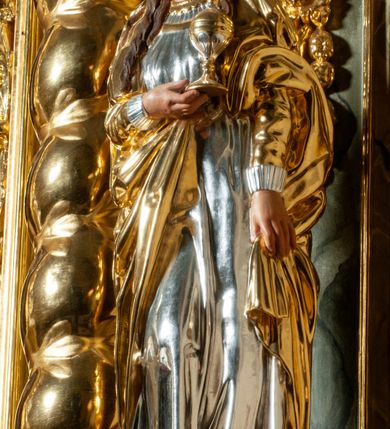 Zdjęcie nr 3: Pełnoplastyczna, drążona od tyłu, drewniana rzeźba stojąca po prawej stronie ołtarza głównego. Maria Magdalena stoi w lekkim kontrapoście, z głową przechyloną na prawo. W prawym ręku trzyma puszkę na wonności, lewą, opuszczoną wzdłuż ciała, podtrzymuje draperie szat. Ma owalną twarz o pełnych policzkach i wysokim czole. Niewielkie oczy i usta, wąskie brwi. Długie, falowane włosy opadają jej na oba ramiona. Jest ubrana w sięgającą ziemi, srebrzoną suknię oraz obfity, długi, złocony płaszcz, którego poła okrywa głowę postaci. U dołu, spod szat, widoczne są czubki jej butów. Włosy, karnacja oraz buty polichromowane; szaty srebrzone i złocone.