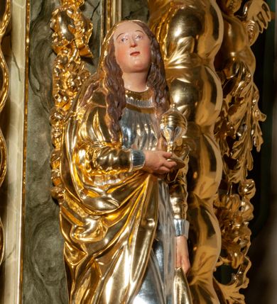 Zdjęcie nr 1: Pełnoplastyczna, drążona od tyłu, drewniana rzeźba stojąca po prawej stronie ołtarza głównego. Maria Magdalena stoi w lekkim kontrapoście, z głową przechyloną na prawo. W prawym ręku trzyma puszkę na wonności, lewą, opuszczoną wzdłuż ciała, podtrzymuje draperie szat. Ma owalną twarz o pełnych policzkach i wysokim czole. Niewielkie oczy i usta, wąskie brwi. Długie, falowane włosy opadają jej na oba ramiona. Jest ubrana w sięgającą ziemi, srebrzoną suknię oraz obfity, długi, złocony płaszcz, którego poła okrywa głowę postaci. U dołu, spod szat, widoczne są czubki jej butów. Włosy, karnacja oraz buty polichromowane; szaty srebrzone i złocone.