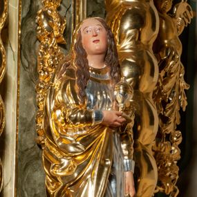 Zdjęcie nr 1: Pełnoplastyczna, drążona od tyłu, drewniana rzeźba stojąca po prawej stronie ołtarza głównego. Maria Magdalena stoi w lekkim kontrapoście, z głową przechyloną na prawo. W prawym ręku trzyma puszkę na wonności, lewą, opuszczoną wzdłuż ciała, podtrzymuje draperie szat. Ma owalną twarz o pełnych policzkach i wysokim czole. Niewielkie oczy i usta, wąskie brwi. Długie, falowane włosy opadają jej na oba ramiona. Jest ubrana w sięgającą ziemi, srebrzoną suknię oraz obfity, długi, złocony płaszcz, którego poła okrywa głowę postaci. U dołu, spod szat, widoczne są czubki jej butów. Włosy, karnacja oraz buty polichromowane; szaty srebrzone i złocone.