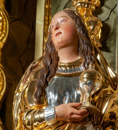 Zdjęcie nr 4: Pełnoplastyczna, drążona od tyłu, drewniana rzeźba stojąca po prawej stronie ołtarza głównego. Maria Magdalena stoi w lekkim kontrapoście, z głową przechyloną na prawo. W prawym ręku trzyma puszkę na wonności, lewą, opuszczoną wzdłuż ciała, podtrzymuje draperie szat. Ma owalną twarz o pełnych policzkach i wysokim czole. Niewielkie oczy i usta, wąskie brwi. Długie, falowane włosy opadają jej na oba ramiona. Jest ubrana w sięgającą ziemi, srebrzoną suknię oraz obfity, długi, złocony płaszcz, którego poła okrywa głowę postaci. U dołu, spod szat, widoczne są czubki jej butów. Włosy, karnacja oraz buty polichromowane; szaty srebrzone i złocone.