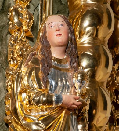 Zdjęcie nr 5: Pełnoplastyczna, drążona od tyłu, drewniana rzeźba stojąca po prawej stronie ołtarza głównego. Maria Magdalena stoi w lekkim kontrapoście, z głową przechyloną na prawo. W prawym ręku trzyma puszkę na wonności, lewą, opuszczoną wzdłuż ciała, podtrzymuje draperie szat. Ma owalną twarz o pełnych policzkach i wysokim czole. Niewielkie oczy i usta, wąskie brwi. Długie, falowane włosy opadają jej na oba ramiona. Jest ubrana w sięgającą ziemi, srebrzoną suknię oraz obfity, długi, złocony płaszcz, którego poła okrywa głowę postaci. U dołu, spod szat, widoczne są czubki jej butów. Włosy, karnacja oraz buty polichromowane; szaty srebrzone i złocone.