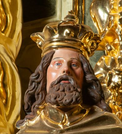 Zdjęcie nr 5: Pełnoplastyczna, wydrążona z tyłu do połowy wysokości, drewniana figura św. Zygmunta, ustawiona po lewej stronie ołtarza głównego. Święty został przedstawiony w pozycji stojącej, z lewą nogą wysuniętą nieco do przodu, ubrany w zbroję płytową, na którą narzucono mu obfity płaszcz spięty pod szyją. W lewej, ugiętej w łokciu i wyciągniętej ku przodowi ręce trzyma jabłko królewskie, prawą wspiera na mieczu przytroczonym do boku. Twarz pociągła, okolona długimi włosami opadającymi na oba ramiona i falującą brodą. Ma pełne, lekko rozchylone usta, prosty nos i przysłonięte grubymi powiekami oczy; na głowie korona. Partie twarzy i włosów polichromowane, szaty i atrybuty władzy królewskiej złocone. Części zbroi (napierśnik i nakolanniki) srebrzone, pozostałe partie złocone.