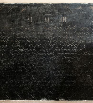 Zdjęcie nr 1: Tablica w kształcie leżącego prostokąta w obramieniu ze stylizowanych liści oplatatających ramę. W narożach rozetki. W górnej części ryty wizerunek uskrzydlonej klepsydry, w dolnej węża połykającego swój ogon. Inskrypcja  ryta, wykonana minuskułową kursywą.
„D(EO) O(PTIMO) M(AXIMO) / Karolinie Macieia z Grabskich Katarzyny / Kwapiszewskich Małżonków, Córce Eufrozyny / Drugiego Imienia, po Siedemnastém lecie, / Zeszłey z tego Swiata w Naypiękniéyszym kwiecie. /  Tysiąc Ośmset dwudziestego i Piątego / Roku a  Listopada dnia Siedemnastego. / Z rąk Rodziców płaczących wyrwanéy Stawiony / I łzami ku wiecznéy pamiątce skropiony. / Tu żałośni Rodzice Córke swą złożyli, /  Wątpiąc czyli Ją Światłu czy Niebu zrodzili, / Lecz, skoro Ją tak prędko Smierć z Oczu porwała, /  Znak nie omylny, że się Niebu podobała. / Przechodniu, co masz na celu duszy zbawienie, / Z mów za Nią choć iedno szczere pozdrowienie”.  
