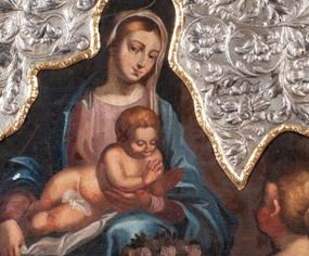 Zdjęcie nr 1: Obraz w kształcie owalu malowany na płótnie naklejonym na deskę. W centrum Matka Boska z Dzieciątkiem na kolanach. Maria w pozycji siedzącej, ukazana całopostaciowo, lewą ręką ugiętą w łokciu podtrzymuje Dzieciątko w okolicy klatki piersiowej. Głowa pochylona nieco w lewą stronę. Twarz o rysach młodej kobiety, oczy brązowe, nos długi, usta wąskie. Karnacja jasna, z rumieńcami na policzkach; włosy jasne, przykryte maforionem. Maria jest ubrana w suknię z długimi rękawami w kolorze jasnoróżowym, na którą zarzucony jest obfity, błękitny płaszcz okrywający ramiona. Spod szat widoczna lewa, bosa stopa. Nad głową malowany nimb, powyżej powtórzony w trybowanej blasze; złocony. Dzieciątko jest nagie, leży na kolanach Matki z głową pochyloną lekko do przodu. Ręce  ma ugięte, rozchylone w geście błogosławieństwa. Włosy ma krótkie, gęste, jasnobrązowe, twarz okrągłą z krótkim nosem, wąskimi ustami i półprzymkniętymi powiekami. Z prawej strony, w dole kompozycji, na pierwszym planie, ukazana klęcząca kobieta. W obu wyciągniętych przed siebie rękach trzyma tacę, na której leżą jasnoróżowe róże. Na głowie ma dekoracyjnie upięty kok, w który wpleciony jest pas materiału. Ubrana jest w ciemnoczerwoną suknię z krótkimi rękawami i szerokim dekoltem. Tło kompozycji jednolite, ciemne. Na górną część obrazu nałożony okład ze srebrnej blachy repusowanej w motywy wici roślinno-kwiatowej. Wewnętrzna krawędź okładu obwiedziona pozłoconym pasem blachy, z repusowanym ornamentem roślinnym. Na krawędzi punca kontrybucyjna „CE”.