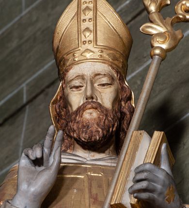 Zdjęcie nr 2: Rzeźba pełnoplastyczna, przyścienna; przedstawienie św. Stanisława Biskupa w całej postaci, frontalnie, w stroju pontyfikalnym. Prawą ręką błogosławi, lewą trzyma księgę i podtrzymuje pastorał. Po jego prawej stronie, u stóp, ukazany Piotrowin w półpostaci, ze złożonymi do modlitwy dłońmi. Karnacje w kolorze naturalnym, szaty pozłocone i srebrzyste.