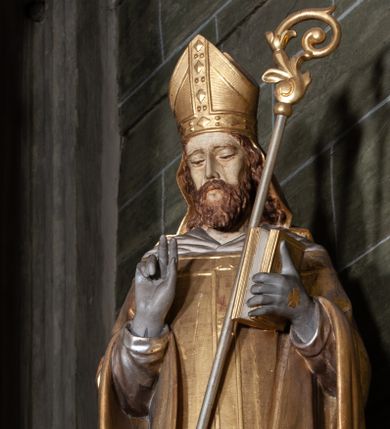 Zdjęcie nr 1: Rzeźba pełnoplastyczna, przyścienna; przedstawienie św. Stanisława Biskupa w całej postaci, frontalnie, w stroju pontyfikalnym. Prawą ręką błogosławi, lewą trzyma księgę i podtrzymuje pastorał. Po jego prawej stronie, u stóp, ukazany Piotrowin w półpostaci, ze złożonymi do modlitwy dłońmi. Karnacje w kolorze naturalnym, szaty pozłocone i srebrzyste.