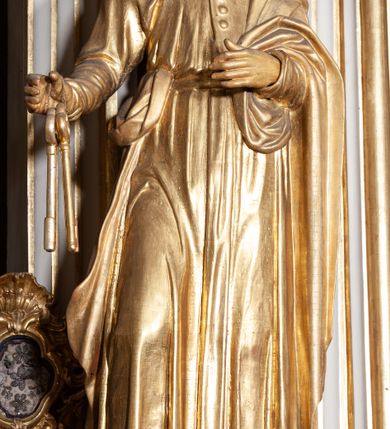 Zdjęcie nr 7: Rzeźba pełnoplastyczna, przyścienna; przedstawienie św. Piotra Apostoła w całej postaci, frontalnie, stoi boso w lekkim kontrapoście, z głową skierowaną lekko w lewo. Twarz starszego mężczyzny, pociągła, z wysokim czołem, okolona wianuszkiem sięgających ramion kręconych włosów i obfitym zarostem. Ręce ugięte w łokciach, w prawej trzyma dwa duże klucze. Ubrany w długą suknię z długimi, wąskimi rękawami, na lewe ramię zarzucony płaszcz przerzucony przez lewą rękę. Cała rzeźba wraz z karnacjami pozłocona.