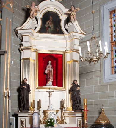Zdjęcie nr 1: Ołtarz architektoniczny, jednoosiowy, jednokondygnacyjny, ze zwieńczeniem. Mensa drewniana, umieszczona na prostopadłościennej skrzyni; antependium z prostokątną płyciną. Nastawa ujęta czworobocznymi, kanelowanymi filarami, ustawionymi ukośnie na tle kanelowanych pilastrów. Filary dźwigają pełne belkowanie i profilowany gzyms, występujące nad nimi. Przy filarach od czoła na wysokich, prostopadłościennych postumentach rzeźby dwóch świętych jezuickich w czarnych sutannach. W polu środkowym nastawy prostokątne nisza ujęta złoconą ramą, w której rzeźba Najświętsze Serce Jezusa.  Zwieńczenie w kształcie aedikuli zamkniętej łukiem półkolistym nadwieszonym i o wklęsłych bokach; pośrodku obraz z przedstawieniem świętego męczennika powtarzający kształt aedikuli. Po bokach, w osiach filarów, odcinki przerwanego przyczółka, na których siedzą dwa putta. Struktura malowana na biało, detale architektoniczne i ornamenty złocone. 