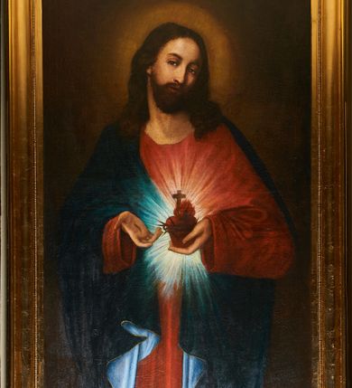Zdjęcie nr 1: Obraz w kształcie stojącego prostokąta w złoconej, profilowanej ramie. Na nim postać Chrystusa ukazanego w ujęciu do kolan, stojącego centralnie, z głową przechyloną w stronę lewego barku, sercem w lewej dłoni i wskazując na nie prawą. Głowa zwrócona w lewo,  wzrok skierowany na widza nos prosty, usta wąskie; twarz okala bujny, ciemnobrązowy zarost, falowane włosy opadają na ramiona i plecy. Wokół głowy świetlisty nimb. Chrystus jest ubrany w czerwoną tunikę z długimi rękawami i granatowy, podbity bielą płaszcz lamowany złotem, który przerzucony jest przez prawy bark. Trzymane w dłoni serce jest otoczone koroną cierniową, zwieńczone płomieniem i krzyżem łacińskim, otacza je jasna gloria promienista. Tło jednolite, ciemne.