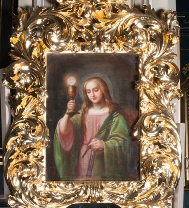 Zdjęcie nr 2: Obraz w kształcie stojącego prostokąta z przedstawieniem św.  Barbary. Święta została ukazana w półpostaci, zwrócona lekko wprawo, wzrok skierowany ma w dół. W prawej, uniesionej przed siebie ręce trzyma kielich z jaśniejącą ponad nim hostią , w lewej, zgiętej w łokciu palmę męczeńską oraz skierowany ostrzem w dół miecz. Twarz owalna o łagodnym wyrazie, jasnej karnacji, z okrągłymi  oczami, prostym nosem, drobnymi ustami okolona jasnymi, delikatnie falującymi się włosami, które opadają na plecy i dekolt; wokół głowy nimb. Święta ubrana w przewiązaną w pasie różową suknię z szerokim dekoltem oraz jasnozielony płaszcz zarzucony na ramiona, który marszczy się na rękawach grubymi fałdami. Przy lewym barku świętej napis „1881 / Wojciech Eljasz”. Tło niemal jednolite, brunatne. Obraz ujęty w ozdobną ramę utworzoną z częściowo ażurowych splotów dość bujnych liści akantu, z wyodrębnionym osobno rodzajem zwieńczenia. W dolnej części prostokątny kartusz ułożony poziomo, zamkniety na krótszych pokach pólkolami, z przedstawieniem otwartej korony, przez którą przechodzą dwie, skrzyżowane gałązki palmowe, wyobrażonych na ciemnym, niemal czarnym tle.