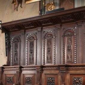 Zdjęcie nr 1: Stalle na rzucie wydłużonego prostokąta, dwurzędowe, pięcioosiowe. Zaplecek wysoki, zwieńczony baldachimem, od dołu poprzedzonym przez wąskie belkowanie, podtrzymywanym po bokach przez dwa wolutowe wsporniki osadzone na hermach. Pole zaplecka dzielone na pięć części, oddzielonych zdwojonymi pilastrami z głowicami zbliżonymi do jońskich; belkowanie przełamuje się na ich osi. W polach pomiędzy pilastrami pionowe prostokątne płyciny zwieńczone półkoliście, w profilowanych obramieniach, na zewnątrz których dodatkowo pasy boniowań. W polach płycin ornament roślinny z główką anielską w centrum, w zwieńczeniach płycin muszle. Siedziska od przodu poprzedzone ścianką z parapetem, która równocześnie pełni funkcję niskiego zaplecka dla drugiego rzędu siedzisk położonych niżej niż górne. Dolny zaplecek podzielony niskimi, hermowymi pilastrami, wspierającymi belkowanie, między pilastrami prostokątne płyciny w profilowanych obramieniach dekorowane rozetami z rautami pośrodku. Siedziska rozdzielone są niskimi podłokietnikami w formie wolut zdobionych cekinamii motywami roślinnymi. Na linii podłokietników, poniżej siedzisk widoczna ich kontynuacja w formie ścianek, u dołu masywna partia cokołowa.