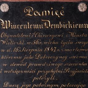 Zdjęcie nr 1: Tablica epitafijna w kształcie stojącego prostokąta, zdobiona w narożach czterema rozetkami z jasnego kamienia. Na tablicy inskrypcja  „Pamięć / Wincentemu Dembickiemu / Obywatelowi i Chirurgowi Miasta / Wieliczki w 56. r(oku) wieku życia swego / w d(nia) 16. Sierpnia 1847. r(oku) zmarłemu / któremu jako Dobroczyńcy swemu / w dowód prawdziwego szacunku / i wdzięczności przychylni Przyjaciele / położyli. / Duszę jego pobożnym polecając / westchnieniom."