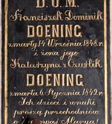 Zdjęcie nr 1: Tablica epitafijna w kształcie stojącego prostokąta, w polu wyznaczonym złotą, malowaną ramką inskrypcja:  „D(EO) O(PTIMO) M(AXIMO) / Franciszek Dominik / DOENING / zmarły 14. Września 1848. r(oku) / i żona jego / Katarzyna z Czurlik / DOENING / zmarła 6. Stycznia 1849. r(oku) / Ich dzieci i wnuki / proszą przechodniów / o Zdrowaś Marya!&quot;