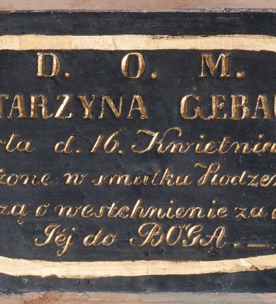 Zdjęcie nr 1: Tablica epitafijna w kształcie leżącego prostokąta. Na tablicy inskrypcja „D(EO) O(PTIMO) M(AXIMO) / KATARZYNA GEBAUER / umarła d(nia) 16. Kwietnia 1856 r(oku) / Pogrążone w smutku Rodzeństwo / proszą o westchnienie za dusze / Jej do BOGA.&quot; Napis ujęto w owalną, złotą, malowaną ramkę. Narożniki wypełniają silnie przestylizowane rozety ujęte z profilu.