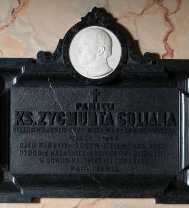 Zdjęcie nr 1: Epitafium w kształcie leżącego prostokąta z profilowanym obramieniem z uszakami. Na osi w górnej części owalny medalion z profilem zmarłego. Pośrodku tablicy inskrypcja: &quot;Pamięci KS(KSIĘDZA) ZYGMUNTA GOLIANA / NIEZRÓWNANYCH CNÓT MĘŻA KAPŁANA, OBYWATELA / *1824_ +1885. / OJCU PARAFII – ODNOWICIELOWI KOŚCIOŁA – / OZDOBIE KAZALNICY – OPIEKUNOWI BIEDNYCH – / W DOWÓD NAJGŁĘBSZEJ CZCI I ŻALU / PARAFIANIE&quot;. W prawym dolnym rogu sygnatura kamieniarza: &quot;E(DWARD) STEHLIK&quot;. W dolnej części medalionu sygnatura: &quot;M(arceli) Guyski / 1886&quot;. 