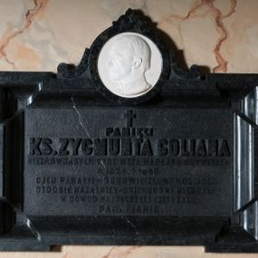 Zdjęcie nr 1: Epitafium w kształcie leżącego prostokąta z profilowanym obramieniem z uszakami. Na osi w górnej części owalny medalion z profilem zmarłego. Pośrodku tablicy inskrypcja: "Pamięci KS(KSIĘDZA) ZYGMUNTA GOLIANA / NIEZRÓWNANYCH CNÓT MĘŻA KAPŁANA, OBYWATELA / *1824_ +1885. / OJCU PARAFII – ODNOWICIELOWI KOŚCIOŁA – / OZDOBIE KAZALNICY – OPIEKUNOWI BIEDNYCH – / W DOWÓD NAJGŁĘBSZEJ CZCI I ŻALU / PARAFIANIE". W prawym dolnym rogu sygnatura kamieniarza: "E(DWARD) STEHLIK". W dolnej części medalionu sygnatura: "M(arceli) Guyski / 1886". 