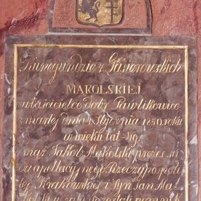Zdjęcie nr 1: Tablica epitafijna w kształcie stojącego prostokąta zwieńczona na osi pełnym łukiem, w którego polu umieszczono herb. Na złotej, dwudzielnej w słup tarczy przedstawiono w prawym polu godło herbu Gryf, a w lewym polu godło herbu Pilawa. Tarczę nakrywa otwarta korona, nad którą znajdują się klejnoty, po prawej stronie – półgryf z trąbą, po lewej – trzy strusie pióra. Na tablicy otoczona złotą, malowaną ramką inskrypcja „Kunegundzie z Gąsiorowskich / MĄKOLSKIEJ / właścicielce dóbr Pawlikowice / zmarłej dnia 4. stycznia 1850. roku / w wieku lat-49. / mąż Jakob Mąkolski prezes są/du apellacyjnego. Rzeczypospoli/tej Krakowskiej i Syn Jan Mą/kolski w żalu pozostali pomnik / ten położyli.”