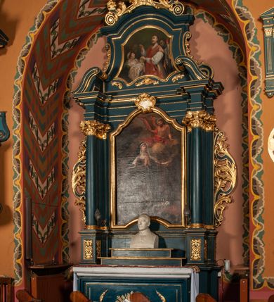 Zdjęcie nr 4: Ołtarz przyścienny, architektoniczny, jednokondygnacyjny, jednoosiowy, ze zwieńczeniem.  Mensa w formie prostopadłościanu. Antepedium proste z płaskorzeźbionym przedstawieniem Baranka Bożego w polu. Retabulum umieszczone na zdwojonym cokole, flankowane kolumnami, ustawionymi na tle zwielokrotnionych pilastrów podtrzymujących wyłamane belkowanie; na osi kolumn przerwany wolutowy przyczółek. W polu głównym nastawy płytka wnęka, ujęte złoconą i profilowaną ramą w kształcie stojącego prostokąta zamkniętego łukiem wklęsło-wypukłym z uskokami. Pośrodku obraz „Św. Kinga”. W górnej części ramy złocony kartusz. Zwieńczenie o delikatnie wklęsłych bokach ujętych spływami wolutowymi, zamknięte łukiem nadwieszonym. Nad nim złocona muszla palmetowa między dwoma spływami wolutowymi. W polu zwieńczenia obraz „Św. Walenty” w ramie o fantazyjnym wykroju. Retabulum flankowane po bokach ażurowymi uszami utworzonymi z liści akantu i przeplatającej je karbowanej wstęgi. Podpory ustawione na bazach, kapitele kompozytowe, trzony kolumn gładkie, natomiast trzony pilastrów kanelowane. Struktura malowana w kolorze ciemnozielonym, ornamenty i detale złocone.

