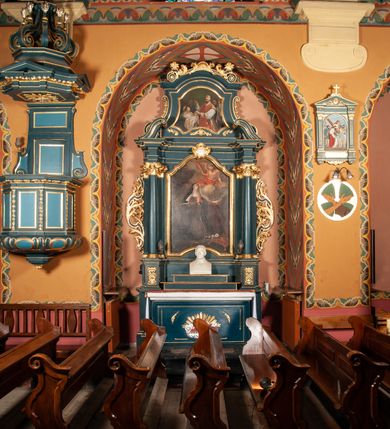 Zdjęcie nr 2: Ołtarz przyścienny, architektoniczny, jednokondygnacyjny, jednoosiowy, ze zwieńczeniem.  Mensa w formie prostopadłościanu. Antepedium proste z płaskorzeźbionym przedstawieniem Baranka Bożego w polu. Retabulum umieszczone na zdwojonym cokole, flankowane kolumnami, ustawionymi na tle zwielokrotnionych pilastrów podtrzymujących wyłamane belkowanie; na osi kolumn przerwany wolutowy przyczółek. W polu głównym nastawy płytka wnęka, ujęte złoconą i profilowaną ramą w kształcie stojącego prostokąta zamkniętego łukiem wklęsło-wypukłym z uskokami. Pośrodku obraz „Św. Kinga”. W górnej części ramy złocony kartusz. Zwieńczenie o delikatnie wklęsłych bokach ujętych spływami wolutowymi, zamknięte łukiem nadwieszonym. Nad nim złocona muszla palmetowa między dwoma spływami wolutowymi. W polu zwieńczenia obraz „Św. Walenty” w ramie o fantazyjnym wykroju. Retabulum flankowane po bokach ażurowymi uszami utworzonymi z liści akantu i przeplatającej je karbowanej wstęgi. Podpory ustawione na bazach, kapitele kompozytowe, trzony kolumn gładkie, natomiast trzony pilastrów kanelowane. Struktura malowana w kolorze ciemnozielonym, ornamenty i detale złocone.

