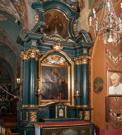 Zdjęcie nr 1: Ołtarz przyścienny, architektoniczny, jednokondygnacyjny, jednoosiowy, ze zwieńczeniem.  Mensa w formie prostopadłościanu. Antepedium malowane: pośrodku medalion otoczony wieńcem z kwiatów. W polu otwarta księga z napisem „SIQUAE/RIS / MIRA/CULA” oraz skrzyżowane dwie gałązki palmowe, kajdany i kule inwalidzkie. Po bokach medalionu wolutowo zakręcona wić roślinna zakończona wazonami z kwiatami. Całość ukazana na ciemnozielonym tle. Tabernakulum w formie prostopadłościennej skrzynki, ustawione na niskim cokole, flankowane parą pilastrów z bazami, kanelowanymi trzonami i kapitelami kompozytowymi podtrzymującymi proste belkowanie z trójkątnym przyczółkiem. Zwieńczenie w formie prostopadłościennego postumentu, na którym ustawiony jest krucyfiks. Drzwiczki w kształcie stojącego prostokąta, zamkniętego łukiem nadwieszonym. W polu monogram IHS, poniżej narzędzia Męki Pańskiej. Nad drzwiczkami, w przyłuczach dwie gałązki róż. Retabulum umieszczone na zdwojonym cokole, flankowane kolumnami, ustawionymi na tle zwielokrotnionych pilastrów podtrzymujących wyłamane belkowanie; na osi kolumn przerwany wolutowy przyczółek. W polu głównym nastawy płytka wnęka, ujęta złoconą i profilowaną ramą w kształcie stojącego prostokąta zamkniętego łukiem wklęsło-wypukłym z uskokami. Pośrodku obraz „Św. Antoni Padewski”, a nad nim kartusz z napisem „S(WIĘTY) ANTONI MÓDL SIĘ ZA NAMI”. W górnej części ramy drugi, mniejszy kartusz z napisem „IHS”. Zwieńczenie o delikatnie wklęsłych bokach ujętych spływami wolutowymi i rzędem kampanul, zamknięte łukiem nadwieszonym. Nad nim złocona muszla palmetowa ujęta dwoma spływami wolutowymi. U szczytu zwieńczenia, po bokach ustawione dwa wazoniki z kwiatami. W polu zwieńczenia obraz „Św. Jan Nepomucen” ujęty w ramę o fantazyjnym wykroju. Podpory ustawione na bazach, kapitele kompozytowe, trzony kolumn gładkie, natomiast trzony pilastrów kanelowane. Struktura malowana w kolorze ciemnozielonym, ornamenty i detale złocone.
