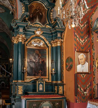 Zdjęcie nr 2: Ołtarz przyścienny, architektoniczny, jednokondygnacyjny, jednoosiowy, ze zwieńczeniem.  Mensa w formie prostopadłościanu. Antepedium malowane: pośrodku medalion otoczony wieńcem z kwiatów. W polu otwarta księga z napisem „SIQUAE/RIS / MIRA/CULA” oraz skrzyżowane dwie gałązki palmowe, kajdany i kule inwalidzkie. Po bokach medalionu wolutowo zakręcona wić roślinna zakończona wazonami z kwiatami. Całość ukazana na ciemnozielonym tle. Tabernakulum w formie prostopadłościennej skrzynki, ustawione na niskim cokole, flankowane parą pilastrów z bazami, kanelowanymi trzonami i kapitelami kompozytowymi podtrzymującymi proste belkowanie z trójkątnym przyczółkiem. Zwieńczenie w formie prostopadłościennego postumentu, na którym ustawiony jest krucyfiks. Drzwiczki w kształcie stojącego prostokąta, zamkniętego łukiem nadwieszonym. W polu monogram IHS, poniżej narzędzia Męki Pańskiej. Nad drzwiczkami, w przyłuczach dwie gałązki róż. Retabulum umieszczone na zdwojonym cokole, flankowane kolumnami, ustawionymi na tle zwielokrotnionych pilastrów podtrzymujących wyłamane belkowanie; na osi kolumn przerwany wolutowy przyczółek. W polu głównym nastawy płytka wnęka, ujęta złoconą i profilowaną ramą w kształcie stojącego prostokąta zamkniętego łukiem wklęsło-wypukłym z uskokami. Pośrodku obraz „Św. Antoni Padewski”, a nad nim kartusz z napisem „S(WIĘTY) ANTONI MÓDL SIĘ ZA NAMI”. W górnej części ramy drugi, mniejszy kartusz z napisem „IHS”. Zwieńczenie o delikatnie wklęsłych bokach ujętych spływami wolutowymi i rzędem kampanul, zamknięte łukiem nadwieszonym. Nad nim złocona muszla palmetowa ujęta dwoma spływami wolutowymi. U szczytu zwieńczenia, po bokach ustawione dwa wazoniki z kwiatami. W polu zwieńczenia obraz „Św. Jan Nepomucen” ujęty w ramę o fantazyjnym wykroju. Podpory ustawione na bazach, kapitele kompozytowe, trzony kolumn gładkie, natomiast trzony pilastrów kanelowane. Struktura malowana w kolorze ciemnozielonym, ornamenty i detale złocone.