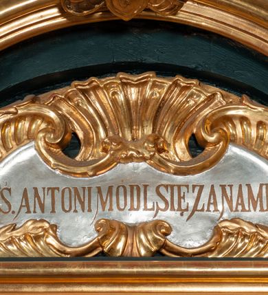 Zdjęcie nr 10: Ołtarz przyścienny, architektoniczny, jednokondygnacyjny, jednoosiowy, ze zwieńczeniem.  Mensa w formie prostopadłościanu. Antepedium malowane: pośrodku medalion otoczony wieńcem z kwiatów. W polu otwarta księga z napisem „SIQUAE/RIS / MIRA/CULA” oraz skrzyżowane dwie gałązki palmowe, kajdany i kule inwalidzkie. Po bokach medalionu wolutowo zakręcona wić roślinna zakończona wazonami z kwiatami. Całość ukazana na ciemnozielonym tle. Tabernakulum w formie prostopadłościennej skrzynki, ustawione na niskim cokole, flankowane parą pilastrów z bazami, kanelowanymi trzonami i kapitelami kompozytowymi podtrzymującymi proste belkowanie z trójkątnym przyczółkiem. Zwieńczenie w formie prostopadłościennego postumentu, na którym ustawiony jest krucyfiks. Drzwiczki w kształcie stojącego prostokąta, zamkniętego łukiem nadwieszonym. W polu monogram IHS, poniżej narzędzia Męki Pańskiej. Nad drzwiczkami, w przyłuczach dwie gałązki róż. Retabulum umieszczone na zdwojonym cokole, flankowane kolumnami, ustawionymi na tle zwielokrotnionych pilastrów podtrzymujących wyłamane belkowanie; na osi kolumn przerwany wolutowy przyczółek. W polu głównym nastawy płytka wnęka, ujęta złoconą i profilowaną ramą w kształcie stojącego prostokąta zamkniętego łukiem wklęsło-wypukłym z uskokami. Pośrodku obraz „Św. Antoni Padewski”, a nad nim kartusz z napisem „S(WIĘTY) ANTONI MÓDL SIĘ ZA NAMI”. W górnej części ramy drugi, mniejszy kartusz z napisem „IHS”. Zwieńczenie o delikatnie wklęsłych bokach ujętych spływami wolutowymi i rzędem kampanul, zamknięte łukiem nadwieszonym. Nad nim złocona muszla palmetowa ujęta dwoma spływami wolutowymi. U szczytu zwieńczenia, po bokach ustawione dwa wazoniki z kwiatami. W polu zwieńczenia obraz „Św. Jan Nepomucen” ujęty w ramę o fantazyjnym wykroju. Podpory ustawione na bazach, kapitele kompozytowe, trzony kolumn gładkie, natomiast trzony pilastrów kanelowane. Struktura malowana w kolorze ciemnozielonym, ornamenty i detale złocone.