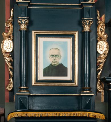 Zdjęcie nr 1: Ołtarz przyścienny, architektoniczny, jednoosiowy, jednokondygnacyjny ze zwieńczeniem. Mensa w formie wysokiego prostopadłościanu. Retabulum ustawione na cokole, ujęte smukłymi kolumnami kompozytowymi stojącymi na bazach. Podpory dźwigają odcinki niepełnego belkowania z rautami w partii fryzu; na nich ustawione niewielkie wazony. W polu prostokątna, złocona rama z wizerunkiem św. Maksymiliana Marii Kolbego. Zwieńczenie o nieregularnym kształcie z bokami ujętymi spływami wolutowymi, zamknięte profilowanym gzymsem w postaci łuku nadwieszonego. Na nim dwie akantowe woluty o układzie przeciwstawnym oraz prosty krzyż. W polu zwieńczenia srebrzony kartusz z kratką wewnątrz. Nastawa ujęta po bokach ażurowymi, akantowymi uszami z motywem woluty. Imposty dekorowane rautami. Struktura malowana na kolor ciemnozielony, ornamenty i detale złocone. 