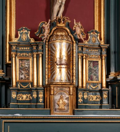 Zdjęcie nr 4: Ołtarz drewniany, dwustronny, obecnie przyścienny, architektoniczny, jednokondygnacyjny ze zwieńczeniem, trójosiowy, z bramkami. Mensa kamienna, prostopadłościenna z antepedium ujętym w profilowaną i złoconą ramę, dekorowaną kimationem jońskim i kampanulami. W polu płaskorzeźbione przedstawienie kielicha z hostią ujętego dwoma otwartymi księgami z napisem na prawej „ECCE / PANIS / ANGE/LORUM”, na lewej „EVAN/GE/LIUM”; liśćmi laurowymi, arma Christi; u podstawy kielicha nałożona korona cierniowa. W dolnych narożach antepedium dekoracja z miękko zawijającej się wstęgi regencyjnej. Tabernakulum o rozbudowanych architektonicznych formach, jednokondygnacyjne, trójosiowe, każda z osi flankowana parą kolumienek i zakończona zwieńczeniem. W osi środkowej tabernakulum metalowe: w dolnej części w formie prostopadłościennej skrzynki z wizerunkiem Chrystusa, w górnej części obrotowe z przedstawieniem Baranka Bożego, zamknięte ozdobnym zwieńczeniem z parą uskrzydlonych putt i koroną w typie zamkniętym. W polach osi bocznych umieszczone za szybką relikwie świętych ujęte prostokątną, złoconą ramą. Retabulum ustawione na wysokim, dwudzielnym cokole, z bramkami o otworach drzwiowych zamkniętych łukiem kotarowym ściętym, nadproża w formie profilowanego gryzmsu. Pole ołtarza, zarówno osi głównej jak i bocznych ujęte jest kolumnami o gładkich trzonach i złoconych kapitalach kompozytowych ustawionych na tle zwieloktrotnionych pilastrów o kanelowanych trzonach. Podpory dźwigają wyłamane na ich osi, pełne belkowanie z wydatnym, silnie profilowanych gzymsem. Na nim fragmenty przyczółka w formie wolut. Pole osi środkowej ze złoconą ramą zamkniętą łukiem wklęsło-wypukłym z uskokiem. W zwieńczeniu ramy wolutowy kartusz o nieregularnym kształcie, z napisem „CONSUMMATUM / EST”. W centrum pola ołtarzowego drewniany krycyfiks. W osi prawej figura św. Kazimierza Królewicza, w osi lewej figura św. Jadwigi Śląskiej. Rzeźby ustawione w niszach, zamkniętych łukiem wklęsło-wypukłym, na rozbudowanych, wolutowych konsolach dekorowanych z przodu kartuszem utworzonym z akantowego wieńca wypełnionego kratką regencyjną; ponad nim girlanda złożona z kampanul i kwiatów. W niszach ponad figurami umieszczone dużych rozmiarów, złocone muszle palmetowe, oraz nieco niżej dwie gałązki akantu. Ponad niszami rozbudowana płaskorzeźbiona dekoracja w formie struktury utworzonej z wolut o karbowanych wypełnieniach, w jej centrum uskrzydlone główki aniołków. Zwieńczenie w formie wklęsło-wypukłej, zamknięte gzymsem w kształcie łuku nadwieszonego, po bokach flankowane dwoma wazonami z kwiatami. W polu obraz św. Michała Archanioła. Kolorystyka ciemnozielona, ze złoceniami w partiach ornamentów oraz w załamaniach profili architektonicznych. Partie cokołu dekorowane płycinami wypełnionymi ornamentem regencyjnym. Według dokumentacji konserwatorskiej na odwrociu ołtarza znajduje się malowana iluzjonistyczna dekoracja przedstawiająca barokowy ołtarz, postacie Matki Boskiej, św. Jana Ewangelisty oraz świętych franciszkańskich.

