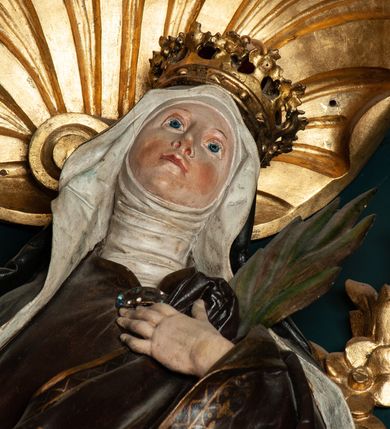 Zdjęcie nr 20: Ołtarz drewniany, dwustronny, obecnie przyścienny, architektoniczny, jednokondygnacyjny ze zwieńczeniem, trójosiowy, z bramkami. Mensa kamienna, prostopadłościenna z antepedium ujętym w profilowaną i złoconą ramę, dekorowaną kimationem jońskim i kampanulami. W polu płaskorzeźbione przedstawienie kielicha z hostią ujętego dwoma otwartymi księgami z napisem na prawej „ECCE / PANIS / ANGE/LORUM”, na lewej „EVAN/GE/LIUM”; liśćmi laurowymi, arma Christi; u podstawy kielicha nałożona korona cierniowa. W dolnych narożach antepedium dekoracja z miękko zawijającej się wstęgi regencyjnej. Tabernakulum o rozbudowanych architektonicznych formach, jednokondygnacyjne, trójosiowe, każda z osi flankowana parą kolumienek i zakończona zwieńczeniem. W osi środkowej tabernakulum metalowe: w dolnej części w formie prostopadłościennej skrzynki z wizerunkiem Chrystusa, w górnej części obrotowe z przedstawieniem Baranka Bożego, zamknięte ozdobnym zwieńczeniem z parą uskrzydlonych putt i koroną w typie zamkniętym. W polach osi bocznych umieszczone za szybką relikwie świętych ujęte prostokątną, złoconą ramą. Retabulum ustawione na wysokim, dwudzielnym cokole, z bramkami o otworach drzwiowych zamkniętych łukiem kotarowym ściętym, nadproża w formie profilowanego gryzmsu. Pole ołtarza, zarówno osi głównej jak i bocznych ujęte jest kolumnami o gładkich trzonach i złoconych kapitalach kompozytowych ustawionych na tle zwieloktrotnionych pilastrów o kanelowanych trzonach. Podpory dźwigają wyłamane na ich osi, pełne belkowanie z wydatnym, silnie profilowanych gzymsem. Na nim fragmenty przyczółka w formie wolut. Pole osi środkowej ze złoconą ramą zamkniętą łukiem wklęsło-wypukłym z uskokiem. W zwieńczeniu ramy wolutowy kartusz o nieregularnym kształcie, z napisem „CONSUMMATUM / EST”. W centrum pola ołtarzowego drewniany krycyfiks. W osi prawej figura św. Kazimierza Królewicza, w osi lewej figura św. Jadwigi Śląskiej. Rzeźby ustawione w niszach, zamkniętych łukiem wklęsło-wypukłym, na rozbudowanych, wolutowych konsolach dekorowanych z przodu kartuszem utworzonym z akantowego wieńca wypełnionego kratką regencyjną; ponad nim girlanda złożona z kampanul i kwiatów. W niszach ponad figurami umieszczone dużych rozmiarów, złocone muszle palmetowe, oraz nieco niżej dwie gałązki akantu. Ponad niszami rozbudowana płaskorzeźbiona dekoracja w formie struktury utworzonej z wolut o karbowanych wypełnieniach, w jej centrum uskrzydlone główki aniołków. Zwieńczenie w formie wklęsło-wypukłej, zamknięte gzymsem w kształcie łuku nadwieszonego, po bokach flankowane dwoma wazonami z kwiatami. W polu obraz św. Michała Archanioła. Kolorystyka ciemnozielona, ze złoceniami w partiach ornamentów oraz w załamaniach profili architektonicznych. Partie cokołu dekorowane płycinami wypełnionymi ornamentem regencyjnym. Według dokumentacji konserwatorskiej na odwrociu ołtarza znajduje się malowana iluzjonistyczna dekoracja przedstawiająca barokowy ołtarz, postacie Matki Boskiej, św. Jana Ewangelisty oraz świętych franciszkańskich.

