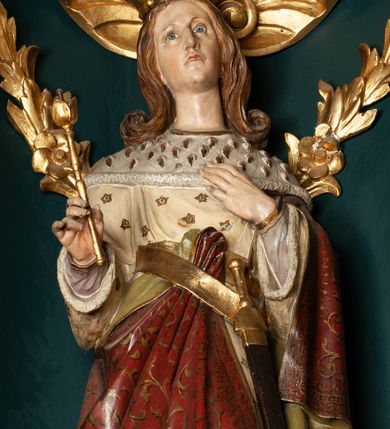 Zdjęcie nr 21: Ołtarz drewniany, dwustronny, obecnie przyścienny, architektoniczny, jednokondygnacyjny ze zwieńczeniem, trójosiowy, z bramkami. Mensa kamienna, prostopadłościenna z antepedium ujętym w profilowaną i złoconą ramę, dekorowaną kimationem jońskim i kampanulami. W polu płaskorzeźbione przedstawienie kielicha z hostią ujętego dwoma otwartymi księgami z napisem na prawej „ECCE / PANIS / ANGE/LORUM”, na lewej „EVAN/GE/LIUM”; liśćmi laurowymi, arma Christi; u podstawy kielicha nałożona korona cierniowa. W dolnych narożach antepedium dekoracja z miękko zawijającej się wstęgi regencyjnej. Tabernakulum o rozbudowanych architektonicznych formach, jednokondygnacyjne, trójosiowe, każda z osi flankowana parą kolumienek i zakończona zwieńczeniem. W osi środkowej tabernakulum metalowe: w dolnej części w formie prostopadłościennej skrzynki z wizerunkiem Chrystusa, w górnej części obrotowe z przedstawieniem Baranka Bożego, zamknięte ozdobnym zwieńczeniem z parą uskrzydlonych putt i koroną w typie zamkniętym. W polach osi bocznych umieszczone za szybką relikwie świętych ujęte prostokątną, złoconą ramą. Retabulum ustawione na wysokim, dwudzielnym cokole, z bramkami o otworach drzwiowych zamkniętych łukiem kotarowym ściętym, nadproża w formie profilowanego gryzmsu. Pole ołtarza, zarówno osi głównej jak i bocznych ujęte jest kolumnami o gładkich trzonach i złoconych kapitalach kompozytowych ustawionych na tle zwieloktrotnionych pilastrów o kanelowanych trzonach. Podpory dźwigają wyłamane na ich osi, pełne belkowanie z wydatnym, silnie profilowanych gzymsem. Na nim fragmenty przyczółka w formie wolut. Pole osi środkowej ze złoconą ramą zamkniętą łukiem wklęsło-wypukłym z uskokiem. W zwieńczeniu ramy wolutowy kartusz o nieregularnym kształcie, z napisem „CONSUMMATUM / EST”. W centrum pola ołtarzowego drewniany krycyfiks. W osi prawej figura św. Kazimierza Królewicza, w osi lewej figura św. Jadwigi Śląskiej. Rzeźby ustawione w niszach, zamkniętych łukiem wklęsło-wypukłym, na rozbudowanych, wolutowych konsolach dekorowanych z przodu kartuszem utworzonym z akantowego wieńca wypełnionego kratką regencyjną; ponad nim girlanda złożona z kampanul i kwiatów. W niszach ponad figurami umieszczone dużych rozmiarów, złocone muszle palmetowe, oraz nieco niżej dwie gałązki akantu. Ponad niszami rozbudowana płaskorzeźbiona dekoracja w formie struktury utworzonej z wolut o karbowanych wypełnieniach, w jej centrum uskrzydlone główki aniołków. Zwieńczenie w formie wklęsło-wypukłej, zamknięte gzymsem w kształcie łuku nadwieszonego, po bokach flankowane dwoma wazonami z kwiatami. W polu obraz św. Michała Archanioła. Kolorystyka ciemnozielona, ze złoceniami w partiach ornamentów oraz w załamaniach profili architektonicznych. Partie cokołu dekorowane płycinami wypełnionymi ornamentem regencyjnym. Według dokumentacji konserwatorskiej na odwrociu ołtarza znajduje się malowana iluzjonistyczna dekoracja przedstawiająca barokowy ołtarz, postacie Matki Boskiej, św. Jana Ewangelisty oraz świętych franciszkańskich.

