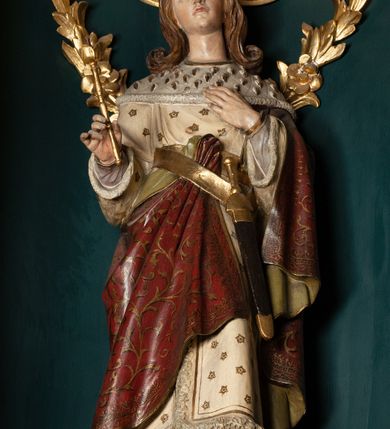 Zdjęcie nr 23: Ołtarz drewniany, dwustronny, obecnie przyścienny, architektoniczny, jednokondygnacyjny ze zwieńczeniem, trójosiowy, z bramkami. Mensa kamienna, prostopadłościenna z antepedium ujętym w profilowaną i złoconą ramę, dekorowaną kimationem jońskim i kampanulami. W polu płaskorzeźbione przedstawienie kielicha z hostią ujętego dwoma otwartymi księgami z napisem na prawej „ECCE / PANIS / ANGE/LORUM”, na lewej „EVAN/GE/LIUM”; liśćmi laurowymi, arma Christi; u podstawy kielicha nałożona korona cierniowa. W dolnych narożach antepedium dekoracja z miękko zawijającej się wstęgi regencyjnej. Tabernakulum o rozbudowanych architektonicznych formach, jednokondygnacyjne, trójosiowe, każda z osi flankowana parą kolumienek i zakończona zwieńczeniem. W osi środkowej tabernakulum metalowe: w dolnej części w formie prostopadłościennej skrzynki z wizerunkiem Chrystusa, w górnej części obrotowe z przedstawieniem Baranka Bożego, zamknięte ozdobnym zwieńczeniem z parą uskrzydlonych putt i koroną w typie zamkniętym. W polach osi bocznych umieszczone za szybką relikwie świętych ujęte prostokątną, złoconą ramą. Retabulum ustawione na wysokim, dwudzielnym cokole, z bramkami o otworach drzwiowych zamkniętych łukiem kotarowym ściętym, nadproża w formie profilowanego gryzmsu. Pole ołtarza, zarówno osi głównej jak i bocznych ujęte jest kolumnami o gładkich trzonach i złoconych kapitalach kompozytowych ustawionych na tle zwieloktrotnionych pilastrów o kanelowanych trzonach. Podpory dźwigają wyłamane na ich osi, pełne belkowanie z wydatnym, silnie profilowanych gzymsem. Na nim fragmenty przyczółka w formie wolut. Pole osi środkowej ze złoconą ramą zamkniętą łukiem wklęsło-wypukłym z uskokiem. W zwieńczeniu ramy wolutowy kartusz o nieregularnym kształcie, z napisem „CONSUMMATUM / EST”. W centrum pola ołtarzowego drewniany krycyfiks. W osi prawej figura św. Kazimierza Królewicza, w osi lewej figura św. Jadwigi Śląskiej. Rzeźby ustawione w niszach, zamkniętych łukiem wklęsło-wypukłym, na rozbudowanych, wolutowych konsolach dekorowanych z przodu kartuszem utworzonym z akantowego wieńca wypełnionego kratką regencyjną; ponad nim girlanda złożona z kampanul i kwiatów. W niszach ponad figurami umieszczone dużych rozmiarów, złocone muszle palmetowe, oraz nieco niżej dwie gałązki akantu. Ponad niszami rozbudowana płaskorzeźbiona dekoracja w formie struktury utworzonej z wolut o karbowanych wypełnieniach, w jej centrum uskrzydlone główki aniołków. Zwieńczenie w formie wklęsło-wypukłej, zamknięte gzymsem w kształcie łuku nadwieszonego, po bokach flankowane dwoma wazonami z kwiatami. W polu obraz św. Michała Archanioła. Kolorystyka ciemnozielona, ze złoceniami w partiach ornamentów oraz w załamaniach profili architektonicznych. Partie cokołu dekorowane płycinami wypełnionymi ornamentem regencyjnym. Według dokumentacji konserwatorskiej na odwrociu ołtarza znajduje się malowana iluzjonistyczna dekoracja przedstawiająca barokowy ołtarz, postacie Matki Boskiej, św. Jana Ewangelisty oraz świętych franciszkańskich.

