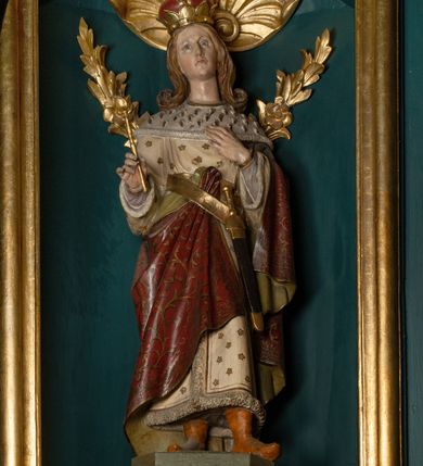 Zdjęcie nr 24: Ołtarz drewniany, dwustronny, obecnie przyścienny, architektoniczny, jednokondygnacyjny ze zwieńczeniem, trójosiowy, z bramkami. Mensa kamienna, prostopadłościenna z antepedium ujętym w profilowaną i złoconą ramę, dekorowaną kimationem jońskim i kampanulami. W polu płaskorzeźbione przedstawienie kielicha z hostią ujętego dwoma otwartymi księgami z napisem na prawej „ECCE / PANIS / ANGE/LORUM”, na lewej „EVAN/GE/LIUM”; liśćmi laurowymi, arma Christi; u podstawy kielicha nałożona korona cierniowa. W dolnych narożach antepedium dekoracja z miękko zawijającej się wstęgi regencyjnej. Tabernakulum o rozbudowanych architektonicznych formach, jednokondygnacyjne, trójosiowe, każda z osi flankowana parą kolumienek i zakończona zwieńczeniem. W osi środkowej tabernakulum metalowe: w dolnej części w formie prostopadłościennej skrzynki z wizerunkiem Chrystusa, w górnej części obrotowe z przedstawieniem Baranka Bożego, zamknięte ozdobnym zwieńczeniem z parą uskrzydlonych putt i koroną w typie zamkniętym. W polach osi bocznych umieszczone za szybką relikwie świętych ujęte prostokątną, złoconą ramą. Retabulum ustawione na wysokim, dwudzielnym cokole, z bramkami o otworach drzwiowych zamkniętych łukiem kotarowym ściętym, nadproża w formie profilowanego gryzmsu. Pole ołtarza, zarówno osi głównej jak i bocznych ujęte jest kolumnami o gładkich trzonach i złoconych kapitalach kompozytowych ustawionych na tle zwieloktrotnionych pilastrów o kanelowanych trzonach. Podpory dźwigają wyłamane na ich osi, pełne belkowanie z wydatnym, silnie profilowanych gzymsem. Na nim fragmenty przyczółka w formie wolut. Pole osi środkowej ze złoconą ramą zamkniętą łukiem wklęsło-wypukłym z uskokiem. W zwieńczeniu ramy wolutowy kartusz o nieregularnym kształcie, z napisem „CONSUMMATUM / EST”. W centrum pola ołtarzowego drewniany krycyfiks. W osi prawej figura św. Kazimierza Królewicza, w osi lewej figura św. Jadwigi Śląskiej. Rzeźby ustawione w niszach, zamkniętych łukiem wklęsło-wypukłym, na rozbudowanych, wolutowych konsolach dekorowanych z przodu kartuszem utworzonym z akantowego wieńca wypełnionego kratką regencyjną; ponad nim girlanda złożona z kampanul i kwiatów. W niszach ponad figurami umieszczone dużych rozmiarów, złocone muszle palmetowe, oraz nieco niżej dwie gałązki akantu. Ponad niszami rozbudowana płaskorzeźbiona dekoracja w formie struktury utworzonej z wolut o karbowanych wypełnieniach, w jej centrum uskrzydlone główki aniołków. Zwieńczenie w formie wklęsło-wypukłej, zamknięte gzymsem w kształcie łuku nadwieszonego, po bokach flankowane dwoma wazonami z kwiatami. W polu obraz św. Michała Archanioła. Kolorystyka ciemnozielona, ze złoceniami w partiach ornamentów oraz w załamaniach profili architektonicznych. Partie cokołu dekorowane płycinami wypełnionymi ornamentem regencyjnym. Według dokumentacji konserwatorskiej na odwrociu ołtarza znajduje się malowana iluzjonistyczna dekoracja przedstawiająca barokowy ołtarz, postacie Matki Boskiej, św. Jana Ewangelisty oraz świętych franciszkańskich.

