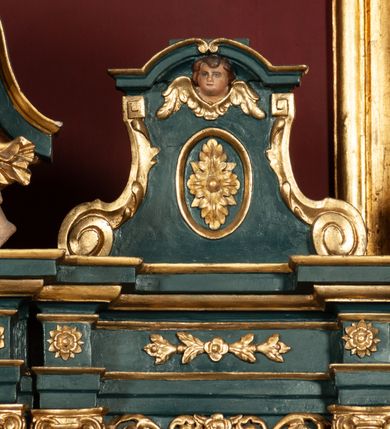 Zdjęcie nr 28: Ołtarz drewniany, dwustronny, obecnie przyścienny, architektoniczny, jednokondygnacyjny ze zwieńczeniem, trójosiowy, z bramkami. Mensa kamienna, prostopadłościenna z antepedium ujętym w profilowaną i złoconą ramę, dekorowaną kimationem jońskim i kampanulami. W polu płaskorzeźbione przedstawienie kielicha z hostią ujętego dwoma otwartymi księgami z napisem na prawej „ECCE / PANIS / ANGE/LORUM”, na lewej „EVAN/GE/LIUM”; liśćmi laurowymi, arma Christi; u podstawy kielicha nałożona korona cierniowa. W dolnych narożach antepedium dekoracja z miękko zawijającej się wstęgi regencyjnej. Tabernakulum o rozbudowanych architektonicznych formach, jednokondygnacyjne, trójosiowe, każda z osi flankowana parą kolumienek i zakończona zwieńczeniem. W osi środkowej tabernakulum metalowe: w dolnej części w formie prostopadłościennej skrzynki z wizerunkiem Chrystusa, w górnej części obrotowe z przedstawieniem Baranka Bożego, zamknięte ozdobnym zwieńczeniem z parą uskrzydlonych putt i koroną w typie zamkniętym. W polach osi bocznych umieszczone za szybką relikwie świętych ujęte prostokątną, złoconą ramą. Retabulum ustawione na wysokim, dwudzielnym cokole, z bramkami o otworach drzwiowych zamkniętych łukiem kotarowym ściętym, nadproża w formie profilowanego gryzmsu. Pole ołtarza, zarówno osi głównej jak i bocznych ujęte jest kolumnami o gładkich trzonach i złoconych kapitalach kompozytowych ustawionych na tle zwieloktrotnionych pilastrów o kanelowanych trzonach. Podpory dźwigają wyłamane na ich osi, pełne belkowanie z wydatnym, silnie profilowanych gzymsem. Na nim fragmenty przyczółka w formie wolut. Pole osi środkowej ze złoconą ramą zamkniętą łukiem wklęsło-wypukłym z uskokiem. W zwieńczeniu ramy wolutowy kartusz o nieregularnym kształcie, z napisem „CONSUMMATUM / EST”. W centrum pola ołtarzowego drewniany krycyfiks. W osi prawej figura św. Kazimierza Królewicza, w osi lewej figura św. Jadwigi Śląskiej. Rzeźby ustawione w niszach, zamkniętych łukiem wklęsło-wypukłym, na rozbudowanych, wolutowych konsolach dekorowanych z przodu kartuszem utworzonym z akantowego wieńca wypełnionego kratką regencyjną; ponad nim girlanda złożona z kampanul i kwiatów. W niszach ponad figurami umieszczone dużych rozmiarów, złocone muszle palmetowe, oraz nieco niżej dwie gałązki akantu. Ponad niszami rozbudowana płaskorzeźbiona dekoracja w formie struktury utworzonej z wolut o karbowanych wypełnieniach, w jej centrum uskrzydlone główki aniołków. Zwieńczenie w formie wklęsło-wypukłej, zamknięte gzymsem w kształcie łuku nadwieszonego, po bokach flankowane dwoma wazonami z kwiatami. W polu obraz św. Michała Archanioła. Kolorystyka ciemnozielona, ze złoceniami w partiach ornamentów oraz w załamaniach profili architektonicznych. Partie cokołu dekorowane płycinami wypełnionymi ornamentem regencyjnym. Według dokumentacji konserwatorskiej na odwrociu ołtarza znajduje się malowana iluzjonistyczna dekoracja przedstawiająca barokowy ołtarz, postacie Matki Boskiej, św. Jana Ewangelisty oraz świętych franciszkańskich.

