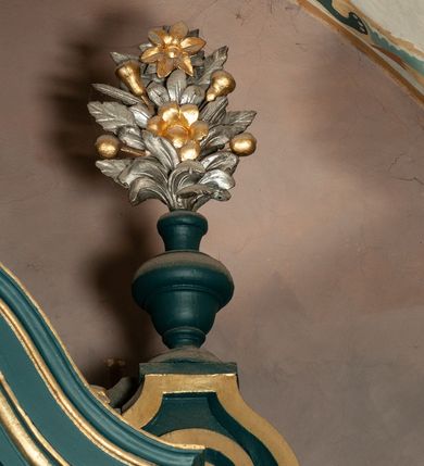 Zdjęcie nr 29: Ołtarz drewniany, dwustronny, obecnie przyścienny, architektoniczny, jednokondygnacyjny ze zwieńczeniem, trójosiowy, z bramkami. Mensa kamienna, prostopadłościenna z antepedium ujętym w profilowaną i złoconą ramę, dekorowaną kimationem jońskim i kampanulami. W polu płaskorzeźbione przedstawienie kielicha z hostią ujętego dwoma otwartymi księgami z napisem na prawej „ECCE / PANIS / ANGE/LORUM”, na lewej „EVAN/GE/LIUM”; liśćmi laurowymi, arma Christi; u podstawy kielicha nałożona korona cierniowa. W dolnych narożach antepedium dekoracja z miękko zawijającej się wstęgi regencyjnej. Tabernakulum o rozbudowanych architektonicznych formach, jednokondygnacyjne, trójosiowe, każda z osi flankowana parą kolumienek i zakończona zwieńczeniem. W osi środkowej tabernakulum metalowe: w dolnej części w formie prostopadłościennej skrzynki z wizerunkiem Chrystusa, w górnej części obrotowe z przedstawieniem Baranka Bożego, zamknięte ozdobnym zwieńczeniem z parą uskrzydlonych putt i koroną w typie zamkniętym. W polach osi bocznych umieszczone za szybką relikwie świętych ujęte prostokątną, złoconą ramą. Retabulum ustawione na wysokim, dwudzielnym cokole, z bramkami o otworach drzwiowych zamkniętych łukiem kotarowym ściętym, nadproża w formie profilowanego gryzmsu. Pole ołtarza, zarówno osi głównej jak i bocznych ujęte jest kolumnami o gładkich trzonach i złoconych kapitalach kompozytowych ustawionych na tle zwieloktrotnionych pilastrów o kanelowanych trzonach. Podpory dźwigają wyłamane na ich osi, pełne belkowanie z wydatnym, silnie profilowanych gzymsem. Na nim fragmenty przyczółka w formie wolut. Pole osi środkowej ze złoconą ramą zamkniętą łukiem wklęsło-wypukłym z uskokiem. W zwieńczeniu ramy wolutowy kartusz o nieregularnym kształcie, z napisem „CONSUMMATUM / EST”. W centrum pola ołtarzowego drewniany krycyfiks. W osi prawej figura św. Kazimierza Królewicza, w osi lewej figura św. Jadwigi Śląskiej. Rzeźby ustawione w niszach, zamkniętych łukiem wklęsło-wypukłym, na rozbudowanych, wolutowych konsolach dekorowanych z przodu kartuszem utworzonym z akantowego wieńca wypełnionego kratką regencyjną; ponad nim girlanda złożona z kampanul i kwiatów. W niszach ponad figurami umieszczone dużych rozmiarów, złocone muszle palmetowe, oraz nieco niżej dwie gałązki akantu. Ponad niszami rozbudowana płaskorzeźbiona dekoracja w formie struktury utworzonej z wolut o karbowanych wypełnieniach, w jej centrum uskrzydlone główki aniołków. Zwieńczenie w formie wklęsło-wypukłej, zamknięte gzymsem w kształcie łuku nadwieszonego, po bokach flankowane dwoma wazonami z kwiatami. W polu obraz św. Michała Archanioła. Kolorystyka ciemnozielona, ze złoceniami w partiach ornamentów oraz w załamaniach profili architektonicznych. Partie cokołu dekorowane płycinami wypełnionymi ornamentem regencyjnym. Według dokumentacji konserwatorskiej na odwrociu ołtarza znajduje się malowana iluzjonistyczna dekoracja przedstawiająca barokowy ołtarz, postacie Matki Boskiej, św. Jana Ewangelisty oraz świętych franciszkańskich.

