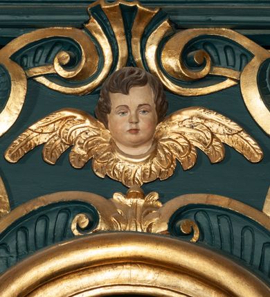 Zdjęcie nr 34: Ołtarz drewniany, dwustronny, obecnie przyścienny, architektoniczny, jednokondygnacyjny ze zwieńczeniem, trójosiowy, z bramkami. Mensa kamienna, prostopadłościenna z antepedium ujętym w profilowaną i złoconą ramę, dekorowaną kimationem jońskim i kampanulami. W polu płaskorzeźbione przedstawienie kielicha z hostią ujętego dwoma otwartymi księgami z napisem na prawej „ECCE / PANIS / ANGE/LORUM”, na lewej „EVAN/GE/LIUM”; liśćmi laurowymi, arma Christi; u podstawy kielicha nałożona korona cierniowa. W dolnych narożach antepedium dekoracja z miękko zawijającej się wstęgi regencyjnej. Tabernakulum o rozbudowanych architektonicznych formach, jednokondygnacyjne, trójosiowe, każda z osi flankowana parą kolumienek i zakończona zwieńczeniem. W osi środkowej tabernakulum metalowe: w dolnej części w formie prostopadłościennej skrzynki z wizerunkiem Chrystusa, w górnej części obrotowe z przedstawieniem Baranka Bożego, zamknięte ozdobnym zwieńczeniem z parą uskrzydlonych putt i koroną w typie zamkniętym. W polach osi bocznych umieszczone za szybką relikwie świętych ujęte prostokątną, złoconą ramą. Retabulum ustawione na wysokim, dwudzielnym cokole, z bramkami o otworach drzwiowych zamkniętych łukiem kotarowym ściętym, nadproża w formie profilowanego gryzmsu. Pole ołtarza, zarówno osi głównej jak i bocznych ujęte jest kolumnami o gładkich trzonach i złoconych kapitalach kompozytowych ustawionych na tle zwieloktrotnionych pilastrów o kanelowanych trzonach. Podpory dźwigają wyłamane na ich osi, pełne belkowanie z wydatnym, silnie profilowanych gzymsem. Na nim fragmenty przyczółka w formie wolut. Pole osi środkowej ze złoconą ramą zamkniętą łukiem wklęsło-wypukłym z uskokiem. W zwieńczeniu ramy wolutowy kartusz o nieregularnym kształcie, z napisem „CONSUMMATUM / EST”. W centrum pola ołtarzowego drewniany krycyfiks. W osi prawej figura św. Kazimierza Królewicza, w osi lewej figura św. Jadwigi Śląskiej. Rzeźby ustawione w niszach, zamkniętych łukiem wklęsło-wypukłym, na rozbudowanych, wolutowych konsolach dekorowanych z przodu kartuszem utworzonym z akantowego wieńca wypełnionego kratką regencyjną; ponad nim girlanda złożona z kampanul i kwiatów. W niszach ponad figurami umieszczone dużych rozmiarów, złocone muszle palmetowe, oraz nieco niżej dwie gałązki akantu. Ponad niszami rozbudowana płaskorzeźbiona dekoracja w formie struktury utworzonej z wolut o karbowanych wypełnieniach, w jej centrum uskrzydlone główki aniołków. Zwieńczenie w formie wklęsło-wypukłej, zamknięte gzymsem w kształcie łuku nadwieszonego, po bokach flankowane dwoma wazonami z kwiatami. W polu obraz św. Michała Archanioła. Kolorystyka ciemnozielona, ze złoceniami w partiach ornamentów oraz w załamaniach profili architektonicznych. Partie cokołu dekorowane płycinami wypełnionymi ornamentem regencyjnym. Według dokumentacji konserwatorskiej na odwrociu ołtarza znajduje się malowana iluzjonistyczna dekoracja przedstawiająca barokowy ołtarz, postacie Matki Boskiej, św. Jana Ewangelisty oraz świętych franciszkańskich.

