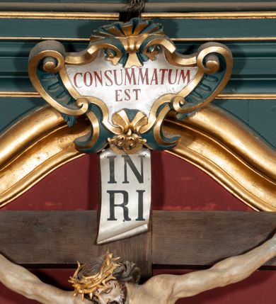 Zdjęcie nr 40: Ołtarz drewniany, dwustronny, obecnie przyścienny, architektoniczny, jednokondygnacyjny ze zwieńczeniem, trójosiowy, z bramkami. Mensa kamienna, prostopadłościenna z antepedium ujętym w profilowaną i złoconą ramę, dekorowaną kimationem jońskim i kampanulami. W polu płaskorzeźbione przedstawienie kielicha z hostią ujętego dwoma otwartymi księgami z napisem na prawej „ECCE / PANIS / ANGE/LORUM”, na lewej „EVAN/GE/LIUM”; liśćmi laurowymi, arma Christi; u podstawy kielicha nałożona korona cierniowa. W dolnych narożach antepedium dekoracja z miękko zawijającej się wstęgi regencyjnej. Tabernakulum o rozbudowanych architektonicznych formach, jednokondygnacyjne, trójosiowe, każda z osi flankowana parą kolumienek i zakończona zwieńczeniem. W osi środkowej tabernakulum metalowe: w dolnej części w formie prostopadłościennej skrzynki z wizerunkiem Chrystusa, w górnej części obrotowe z przedstawieniem Baranka Bożego, zamknięte ozdobnym zwieńczeniem z parą uskrzydlonych putt i koroną w typie zamkniętym. W polach osi bocznych umieszczone za szybką relikwie świętych ujęte prostokątną, złoconą ramą. Retabulum ustawione na wysokim, dwudzielnym cokole, z bramkami o otworach drzwiowych zamkniętych łukiem kotarowym ściętym, nadproża w formie profilowanego gryzmsu. Pole ołtarza, zarówno osi głównej jak i bocznych ujęte jest kolumnami o gładkich trzonach i złoconych kapitalach kompozytowych ustawionych na tle zwieloktrotnionych pilastrów o kanelowanych trzonach. Podpory dźwigają wyłamane na ich osi, pełne belkowanie z wydatnym, silnie profilowanych gzymsem. Na nim fragmenty przyczółka w formie wolut. Pole osi środkowej ze złoconą ramą zamkniętą łukiem wklęsło-wypukłym z uskokiem. W zwieńczeniu ramy wolutowy kartusz o nieregularnym kształcie, z napisem „CONSUMMATUM / EST”. W centrum pola ołtarzowego drewniany krycyfiks. W osi prawej figura św. Kazimierza Królewicza, w osi lewej figura św. Jadwigi Śląskiej. Rzeźby ustawione w niszach, zamkniętych łukiem wklęsło-wypukłym, na rozbudowanych, wolutowych konsolach dekorowanych z przodu kartuszem utworzonym z akantowego wieńca wypełnionego kratką regencyjną; ponad nim girlanda złożona z kampanul i kwiatów. W niszach ponad figurami umieszczone dużych rozmiarów, złocone muszle palmetowe, oraz nieco niżej dwie gałązki akantu. Ponad niszami rozbudowana płaskorzeźbiona dekoracja w formie struktury utworzonej z wolut o karbowanych wypełnieniach, w jej centrum uskrzydlone główki aniołków. Zwieńczenie w formie wklęsło-wypukłej, zamknięte gzymsem w kształcie łuku nadwieszonego, po bokach flankowane dwoma wazonami z kwiatami. W polu obraz św. Michała Archanioła. Kolorystyka ciemnozielona, ze złoceniami w partiach ornamentów oraz w załamaniach profili architektonicznych. Partie cokołu dekorowane płycinami wypełnionymi ornamentem regencyjnym. Według dokumentacji konserwatorskiej na odwrociu ołtarza znajduje się malowana iluzjonistyczna dekoracja przedstawiająca barokowy ołtarz, postacie Matki Boskiej, św. Jana Ewangelisty oraz świętych franciszkańskich.

