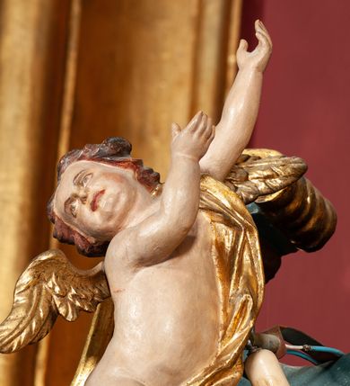 Zdjęcie nr 45: Ołtarz drewniany, dwustronny, obecnie przyścienny, architektoniczny, jednokondygnacyjny ze zwieńczeniem, trójosiowy, z bramkami. Mensa kamienna, prostopadłościenna z antepedium ujętym w profilowaną i złoconą ramę, dekorowaną kimationem jońskim i kampanulami. W polu płaskorzeźbione przedstawienie kielicha z hostią ujętego dwoma otwartymi księgami z napisem na prawej „ECCE / PANIS / ANGE/LORUM”, na lewej „EVAN/GE/LIUM”; liśćmi laurowymi, arma Christi; u podstawy kielicha nałożona korona cierniowa. W dolnych narożach antepedium dekoracja z miękko zawijającej się wstęgi regencyjnej. Tabernakulum o rozbudowanych architektonicznych formach, jednokondygnacyjne, trójosiowe, każda z osi flankowana parą kolumienek i zakończona zwieńczeniem. W osi środkowej tabernakulum metalowe: w dolnej części w formie prostopadłościennej skrzynki z wizerunkiem Chrystusa, w górnej części obrotowe z przedstawieniem Baranka Bożego, zamknięte ozdobnym zwieńczeniem z parą uskrzydlonych putt i koroną w typie zamkniętym. W polach osi bocznych umieszczone za szybką relikwie świętych ujęte prostokątną, złoconą ramą. Retabulum ustawione na wysokim, dwudzielnym cokole, z bramkami o otworach drzwiowych zamkniętych łukiem kotarowym ściętym, nadproża w formie profilowanego gryzmsu. Pole ołtarza, zarówno osi głównej jak i bocznych ujęte jest kolumnami o gładkich trzonach i złoconych kapitalach kompozytowych ustawionych na tle zwieloktrotnionych pilastrów o kanelowanych trzonach. Podpory dźwigają wyłamane na ich osi, pełne belkowanie z wydatnym, silnie profilowanych gzymsem. Na nim fragmenty przyczółka w formie wolut. Pole osi środkowej ze złoconą ramą zamkniętą łukiem wklęsło-wypukłym z uskokiem. W zwieńczeniu ramy wolutowy kartusz o nieregularnym kształcie, z napisem „CONSUMMATUM / EST”. W centrum pola ołtarzowego drewniany krycyfiks. W osi prawej figura św. Kazimierza Królewicza, w osi lewej figura św. Jadwigi Śląskiej. Rzeźby ustawione w niszach, zamkniętych łukiem wklęsło-wypukłym, na rozbudowanych, wolutowych konsolach dekorowanych z przodu kartuszem utworzonym z akantowego wieńca wypełnionego kratką regencyjną; ponad nim girlanda złożona z kampanul i kwiatów. W niszach ponad figurami umieszczone dużych rozmiarów, złocone muszle palmetowe, oraz nieco niżej dwie gałązki akantu. Ponad niszami rozbudowana płaskorzeźbiona dekoracja w formie struktury utworzonej z wolut o karbowanych wypełnieniach, w jej centrum uskrzydlone główki aniołków. Zwieńczenie w formie wklęsło-wypukłej, zamknięte gzymsem w kształcie łuku nadwieszonego, po bokach flankowane dwoma wazonami z kwiatami. W polu obraz św. Michała Archanioła. Kolorystyka ciemnozielona, ze złoceniami w partiach ornamentów oraz w załamaniach profili architektonicznych. Partie cokołu dekorowane płycinami wypełnionymi ornamentem regencyjnym. Według dokumentacji konserwatorskiej na odwrociu ołtarza znajduje się malowana iluzjonistyczna dekoracja przedstawiająca barokowy ołtarz, postacie Matki Boskiej, św. Jana Ewangelisty oraz świętych franciszkańskich.

