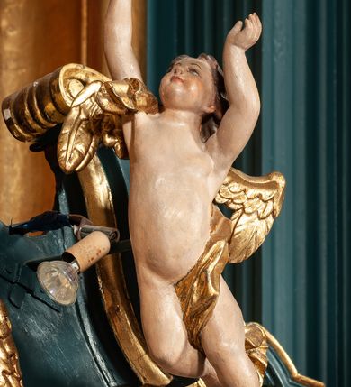 Zdjęcie nr 47: Ołtarz drewniany, dwustronny, obecnie przyścienny, architektoniczny, jednokondygnacyjny ze zwieńczeniem, trójosiowy, z bramkami. Mensa kamienna, prostopadłościenna z antepedium ujętym w profilowaną i złoconą ramę, dekorowaną kimationem jońskim i kampanulami. W polu płaskorzeźbione przedstawienie kielicha z hostią ujętego dwoma otwartymi księgami z napisem na prawej „ECCE / PANIS / ANGE/LORUM”, na lewej „EVAN/GE/LIUM”; liśćmi laurowymi, arma Christi; u podstawy kielicha nałożona korona cierniowa. W dolnych narożach antepedium dekoracja z miękko zawijającej się wstęgi regencyjnej. Tabernakulum o rozbudowanych architektonicznych formach, jednokondygnacyjne, trójosiowe, każda z osi flankowana parą kolumienek i zakończona zwieńczeniem. W osi środkowej tabernakulum metalowe: w dolnej części w formie prostopadłościennej skrzynki z wizerunkiem Chrystusa, w górnej części obrotowe z przedstawieniem Baranka Bożego, zamknięte ozdobnym zwieńczeniem z parą uskrzydlonych putt i koroną w typie zamkniętym. W polach osi bocznych umieszczone za szybką relikwie świętych ujęte prostokątną, złoconą ramą. Retabulum ustawione na wysokim, dwudzielnym cokole, z bramkami o otworach drzwiowych zamkniętych łukiem kotarowym ściętym, nadproża w formie profilowanego gryzmsu. Pole ołtarza, zarówno osi głównej jak i bocznych ujęte jest kolumnami o gładkich trzonach i złoconych kapitalach kompozytowych ustawionych na tle zwieloktrotnionych pilastrów o kanelowanych trzonach. Podpory dźwigają wyłamane na ich osi, pełne belkowanie z wydatnym, silnie profilowanych gzymsem. Na nim fragmenty przyczółka w formie wolut. Pole osi środkowej ze złoconą ramą zamkniętą łukiem wklęsło-wypukłym z uskokiem. W zwieńczeniu ramy wolutowy kartusz o nieregularnym kształcie, z napisem „CONSUMMATUM / EST”. W centrum pola ołtarzowego drewniany krycyfiks. W osi prawej figura św. Kazimierza Królewicza, w osi lewej figura św. Jadwigi Śląskiej. Rzeźby ustawione w niszach, zamkniętych łukiem wklęsło-wypukłym, na rozbudowanych, wolutowych konsolach dekorowanych z przodu kartuszem utworzonym z akantowego wieńca wypełnionego kratką regencyjną; ponad nim girlanda złożona z kampanul i kwiatów. W niszach ponad figurami umieszczone dużych rozmiarów, złocone muszle palmetowe, oraz nieco niżej dwie gałązki akantu. Ponad niszami rozbudowana płaskorzeźbiona dekoracja w formie struktury utworzonej z wolut o karbowanych wypełnieniach, w jej centrum uskrzydlone główki aniołków. Zwieńczenie w formie wklęsło-wypukłej, zamknięte gzymsem w kształcie łuku nadwieszonego, po bokach flankowane dwoma wazonami z kwiatami. W polu obraz św. Michała Archanioła. Kolorystyka ciemnozielona, ze złoceniami w partiach ornamentów oraz w załamaniach profili architektonicznych. Partie cokołu dekorowane płycinami wypełnionymi ornamentem regencyjnym. Według dokumentacji konserwatorskiej na odwrociu ołtarza znajduje się malowana iluzjonistyczna dekoracja przedstawiająca barokowy ołtarz, postacie Matki Boskiej, św. Jana Ewangelisty oraz świętych franciszkańskich.

