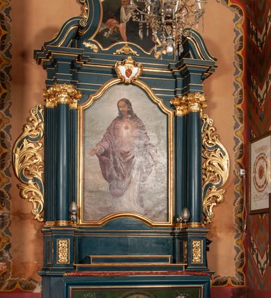 Zdjęcie nr 2: Ołtarz przyścienny, architektoniczny, jednokondygnacyjny, jednoosiowy, ze zwieńczeniem. Mensa w formie prostopadłościanu, antepedium malowane. Pośrodku medalion z wieńca laurowego. W polu wieńca krzyż oraz skrzyżowane narzędzia Męki Pańskiej na tle błękitnego nieba. Po bokach medalionu wolutowo zakręcona wić roślinna zakończona wazonami z kwiatami. Całość ukazana na ciemnozielonym tle. Retabulum umieszczone na zdwojonym cokole, flankowane kolumnami, ustawionymi na tle zwielokrotnionych pilastrów podtrzymujących wyłamane belkowanie; na osi kolumn przerwany wolutowy przyczółek. W polu głównym nastawy płytka wnęka, ujęta złoconą i profilowaną ramą w kształcie stojącego prostokąta zamkniętego łukiem wklęsło-wypukłym z uskokami. Pośrodku obraz „Najświętsze Serce Jezusa”. W górnej części ramy złocony kartusz z gorejącym sercem w polu. Zwieńczenie o delikatnie wklęsłych bokach ujętych spływami wolutowymi, zamknięte łukiem nadwieszonym. Nad nim złocona muszla palmetowa pomiędzy dwoma spływami wolutowymi. W polu zwieńczenia obraz „Św. Jan Kanty” w ramie o fantazyjnym wykroju. Retabulum flankowane po bokach ażurowymi uszami utworzonymi z liści akantu i przeplatającej je karbowanej wstęgi. Podpory ustawione na bazach, kapitele kompozytowe, trzony kolumn gładkie, natomiast trzony pilastrów kanelowane. Struktura malowana w kolorze ciemnozielonym, ornamenty i detale złocone.
