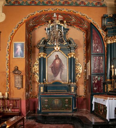 Zdjęcie nr 4: Ołtarz przyścienny, architektoniczny, jednokondygnacyjny, jednoosiowy, ze zwieńczeniem. Mensa w formie prostopadłościanu, antepedium malowane. Pośrodku medalion z wieńca laurowego. W polu wieńca krzyż oraz skrzyżowane narzędzia Męki Pańskiej na tle błękitnego nieba. Po bokach medalionu wolutowo zakręcona wić roślinna zakończona wazonami z kwiatami. Całość ukazana na ciemnozielonym tle. Retabulum umieszczone na zdwojonym cokole, flankowane kolumnami, ustawionymi na tle zwielokrotnionych pilastrów podtrzymujących wyłamane belkowanie; na osi kolumn przerwany wolutowy przyczółek. W polu głównym nastawy płytka wnęka, ujęta złoconą i profilowaną ramą w kształcie stojącego prostokąta zamkniętego łukiem wklęsło-wypukłym z uskokami. Pośrodku obraz „Najświętsze Serce Jezusa”. W górnej części ramy złocony kartusz z gorejącym sercem w polu. Zwieńczenie o delikatnie wklęsłych bokach ujętych spływami wolutowymi, zamknięte łukiem nadwieszonym. Nad nim złocona muszla palmetowa pomiędzy dwoma spływami wolutowymi. W polu zwieńczenia obraz „Św. Jan Kanty” w ramie o fantazyjnym wykroju. Retabulum flankowane po bokach ażurowymi uszami utworzonymi z liści akantu i przeplatającej je karbowanej wstęgi. Podpory ustawione na bazach, kapitele kompozytowe, trzony kolumn gładkie, natomiast trzony pilastrów kanelowane. Struktura malowana w kolorze ciemnozielonym, ornamenty i detale złocone.
