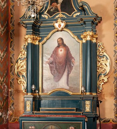 Zdjęcie nr 1: Ołtarz przyścienny, architektoniczny, jednokondygnacyjny, jednoosiowy, ze zwieńczeniem. Mensa w formie prostopadłościanu, antepedium malowane. Pośrodku medalion z wieńca laurowego. W polu wieńca krzyż oraz skrzyżowane narzędzia Męki Pańskiej na tle błękitnego nieba. Po bokach medalionu wolutowo zakręcona wić roślinna zakończona wazonami z kwiatami. Całość ukazana na ciemnozielonym tle. Retabulum umieszczone na zdwojonym cokole, flankowane kolumnami, ustawionymi na tle zwielokrotnionych pilastrów podtrzymujących wyłamane belkowanie; na osi kolumn przerwany wolutowy przyczółek. W polu głównym nastawy płytka wnęka, ujęta złoconą i profilowaną ramą w kształcie stojącego prostokąta zamkniętego łukiem wklęsło-wypukłym z uskokami. Pośrodku obraz „Najświętsze Serce Jezusa”. W górnej części ramy złocony kartusz z gorejącym sercem w polu. Zwieńczenie o delikatnie wklęsłych bokach ujętych spływami wolutowymi, zamknięte łukiem nadwieszonym. Nad nim złocona muszla palmetowa pomiędzy dwoma spływami wolutowymi. W polu zwieńczenia obraz „Św. Jan Kanty” w ramie o fantazyjnym wykroju. Retabulum flankowane po bokach ażurowymi uszami utworzonymi z liści akantu i przeplatającej je karbowanej wstęgi. Podpory ustawione na bazach, kapitele kompozytowe, trzony kolumn gładkie, natomiast trzony pilastrów kanelowane. Struktura malowana w kolorze ciemnozielonym, ornamenty i detale złocone.
