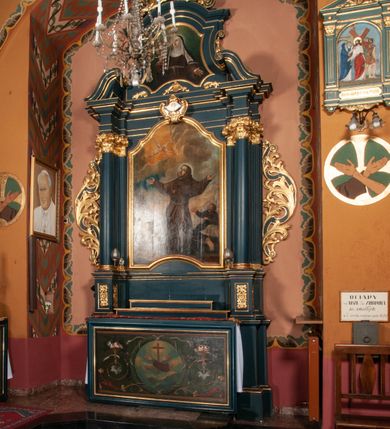 Zdjęcie nr 3: Ołtarz przyścienny, architektoniczny, jednokondygnacyjny, jednoosiowy, ze zwieńczeniem.  Mensa w formie prostopadłościanu. Antepedium malowane. Pośrodku medalion z wieńca laurowego, owiniętego sznurem. W polu wieńca godło zakonu franciszkańskiego (skrzyżowane prawe ręce Chrystusa i św. Franciszka oraz krzyż łaciński) na tle błękitnego nieba. Po bokach medalionu wolutowo zakręcona wić roślinna zakończona wazonami z kwiatami. Całość ukazana na ciemnozielonym tle. Retabulum umieszczone na zdwojonym cokole, flankowane kolumnami, ustawionymi na tle zwielokrotnionych pilastrów podtrzymujących wyłamane belkowanie; na osi kolumn przerwany wolutowy przyczółek. W polu głównym nastawy płytka wnęka, ujęta złoconą i profilowaną ramą w kształcie stojącego prostokąta zamkniętego łukiem wklęsło-wypukłym z uskokami. Pośrodku obraz „Stygmatyzacja św. Franciszka”. W górnej części ramy złocony kartusz z godłem zakonu franciszkańskiego. Zwieńczenie o delikatnie wklęsłych bokach ujętych spływami wolutowymi, zamknięte łukiem nadwieszonym. Nad nim złocona muszla palmetowa pomiędzy dwoma spływami wolutowymi. W polu zwieńczenia obraz św. Klary w ramie o fantazyjnym wykroju. Retabulum flankowane po bokach ażurowymi uszami utworzonymi z liści akantu i przeplatającej je karbowanej wstęgi. Podpory ustawione na bazach, kapitele kompozytowe, trzony kolumn gładkie, natomiast trzony pilastrów kanelowane. Struktura malowana w kolorze ciemnozielonym, ornamenty i detale złocone.
