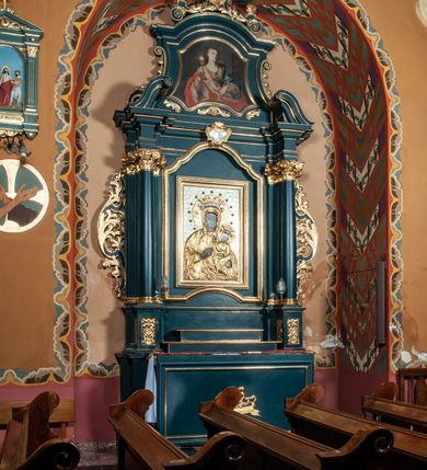 Zdjęcie nr 2: Ołtarz przyścienny, architektoniczny, jednokondygnacyjny, jednoosiowy, ze zwieńczeniem. Mensa w formie prostopadłościanu. Antepedium drewniane, w centrum złocony ormament roślinny oraz banderola.  Retabulum ustawione na zdwojonym cokole, flankowane kolumnami, ustawionych na tle zwielokrotnionych pilastrów podtrzymujących wyłamane belkowanie, na osi kolumn przerwany wolutowy przyczółek. W polu głównym nastawy płytka wnęka, ujęta złoconą i profilowaną ramą w kształcie stojącego prostokąta zamkniętego łukiem wklęsło-wypukłym z uskokami. Pośrodku obraz Matki Boskiej Częstochowskiej. W górnej części ramy złocony kartusz. Zwieńczenie o delikatnie wklęsłych bokach ze spływami wolutowymi, zamknięte łukiem nadwieszonym. Nad nim złocona muszla palmetowa ujęta dwoma spływami wolutowymi. W polu zwieńczenia obraz św. Barbary w ramie o fantazyjnym wykroju. Retabulum flankowane po bokach ażurowymi uszami utworzonymi z liści akantu. Podpory ustawione na bazach, kapitele kompozytowe, trzony kolumn gładkie, natomiast trzony pilastrów kanelowane. Struktura malowana w kolorze ciemnozielonym, ornamenty i detale złocone.